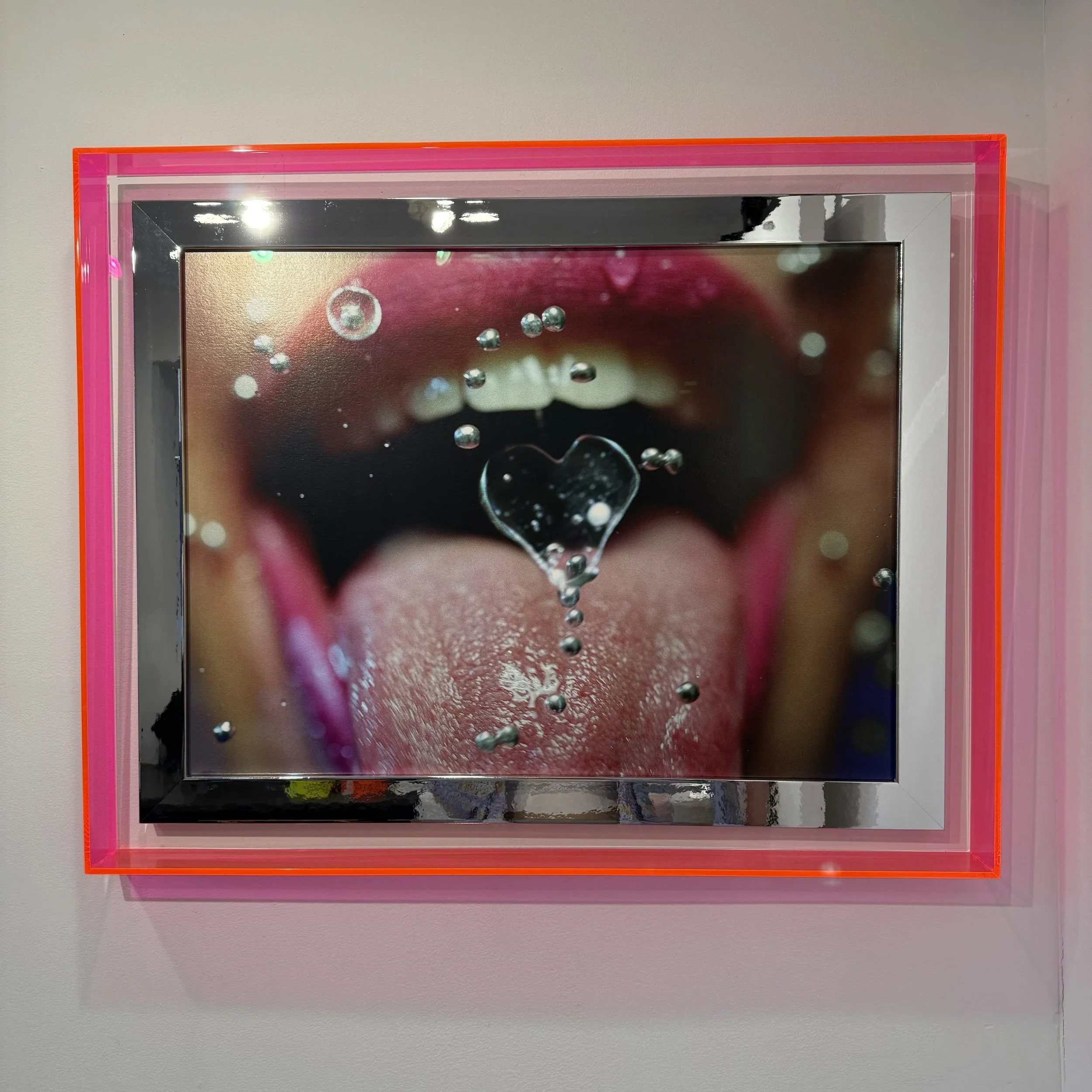 A close-up photograph of a person with open mouth, tongue extended, and a heart-shaped water droplet falling onto their tongue.