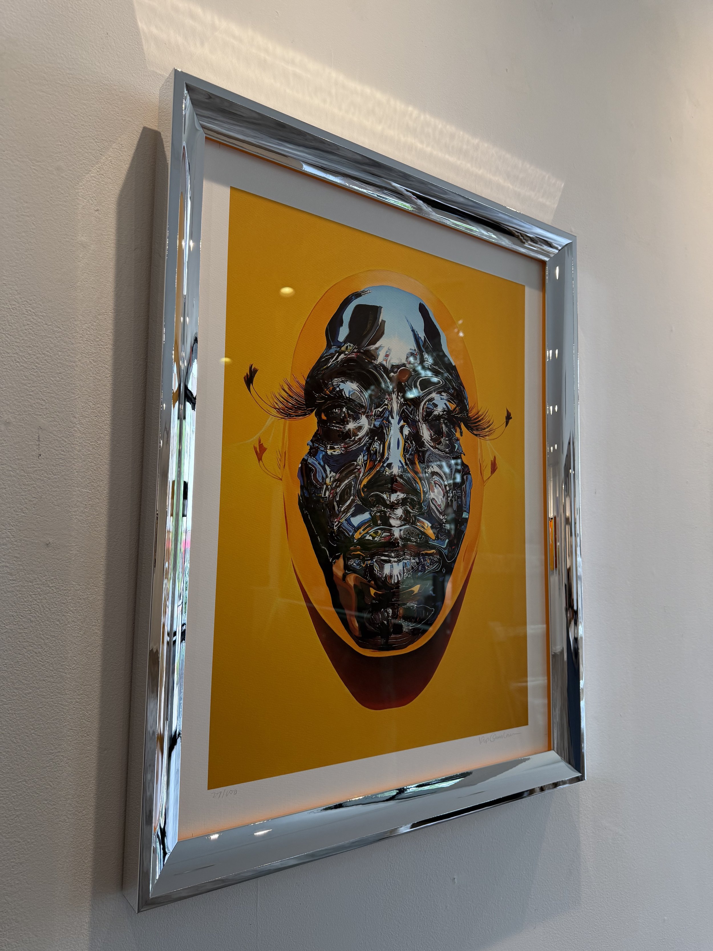 Framed artwork of a surreal human face with floral eyelashes against a yellow background.