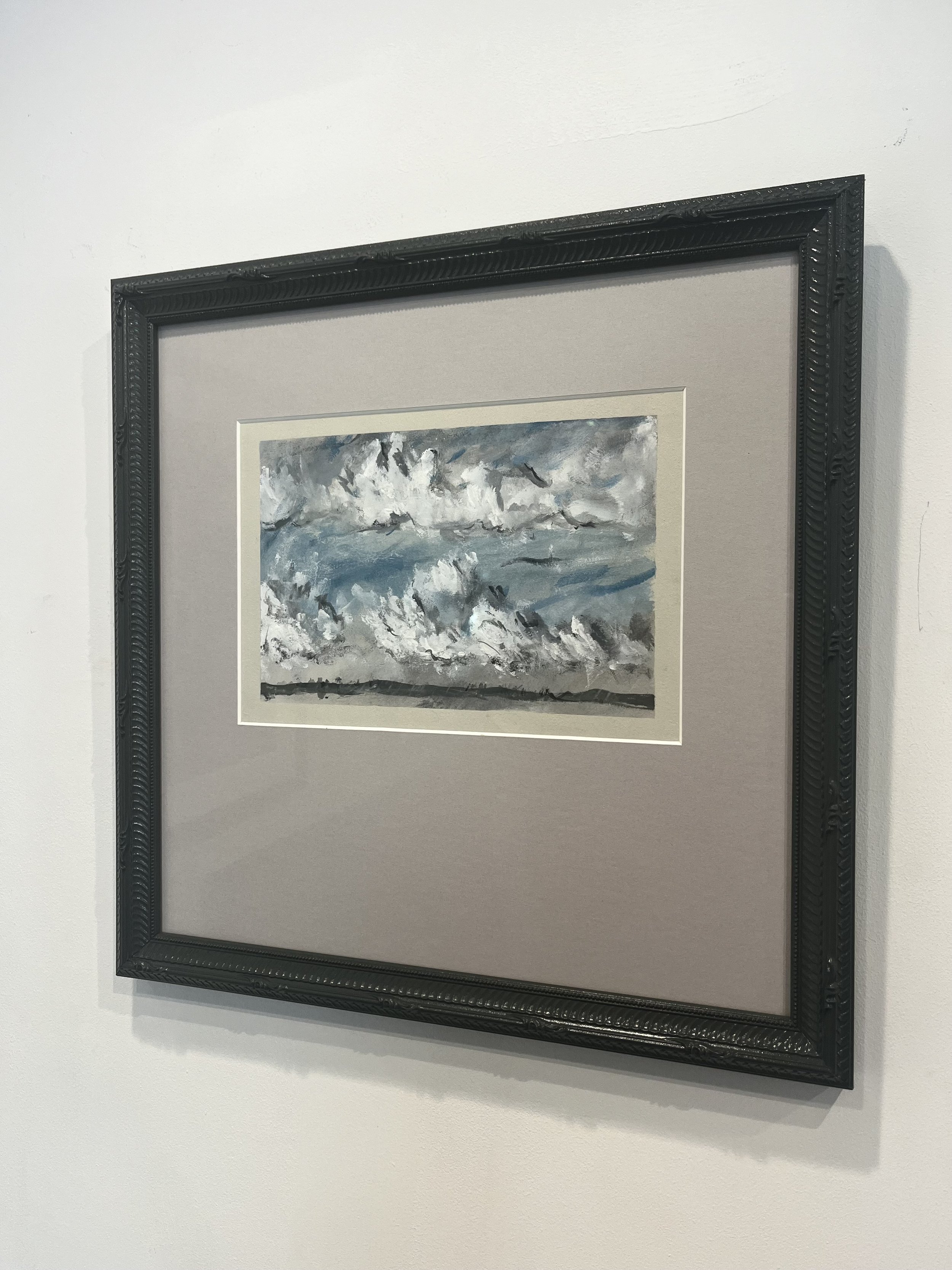 A framed painting of a cloudy sky with waves on the ocean, displayed on a white wall.