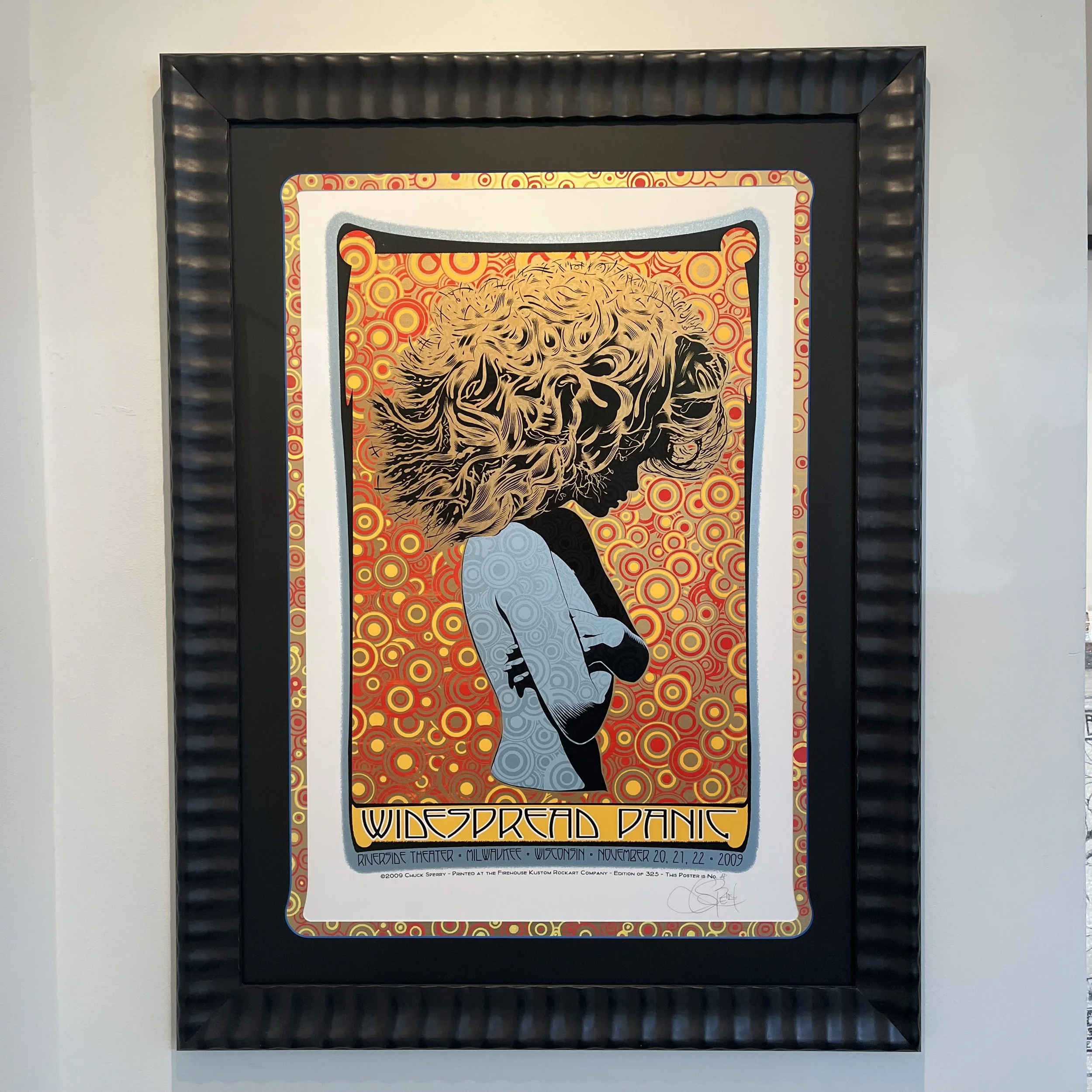 Poster advertising Widespread Panic band concert at Riverside Theater, Milwaukee, Wisconsin, November 20-22, 2009, featuring a stylized profile of a person with a flowing coiffure set against a vibrant, circular-patterned orange background.