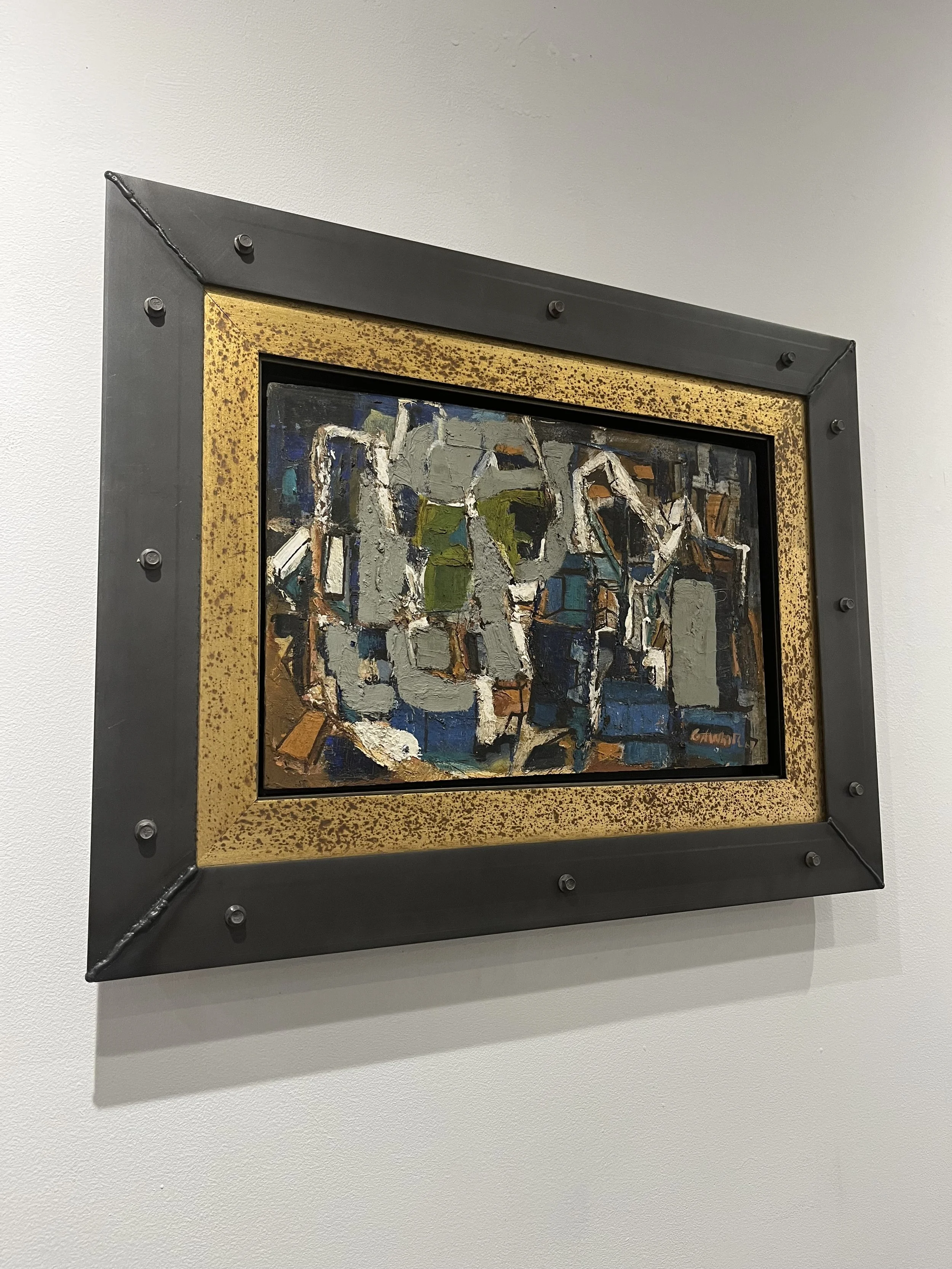 Abstract painting with thick paint strokes in shades of gray, green, blue, white, and orange, framed with a black and gold speckled border, hanging on a white wall.