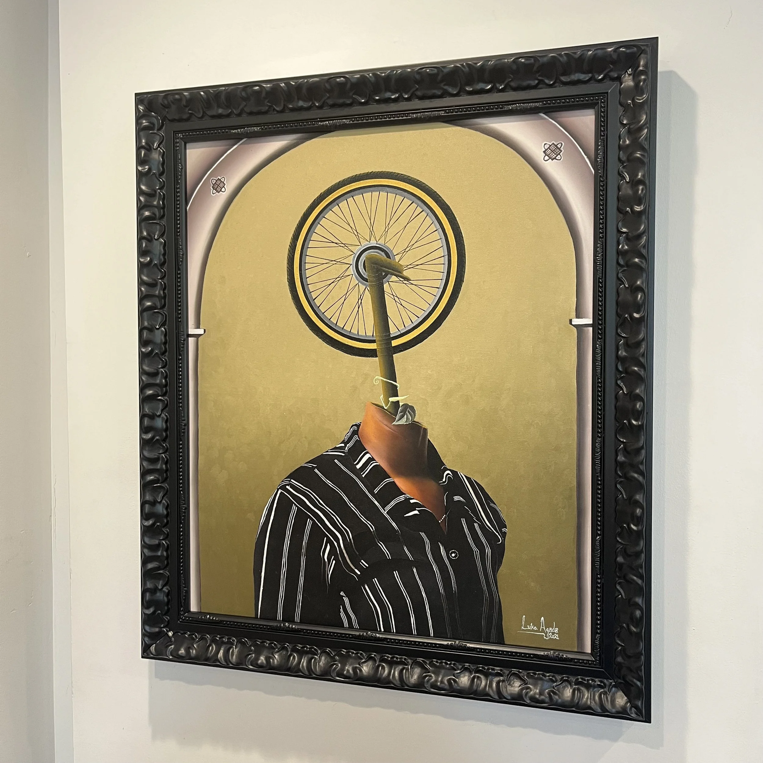 Surreal artwork of a person with a bicycle wheel as a head, wearing a striped shirt, with a yellow background and decorative frame.