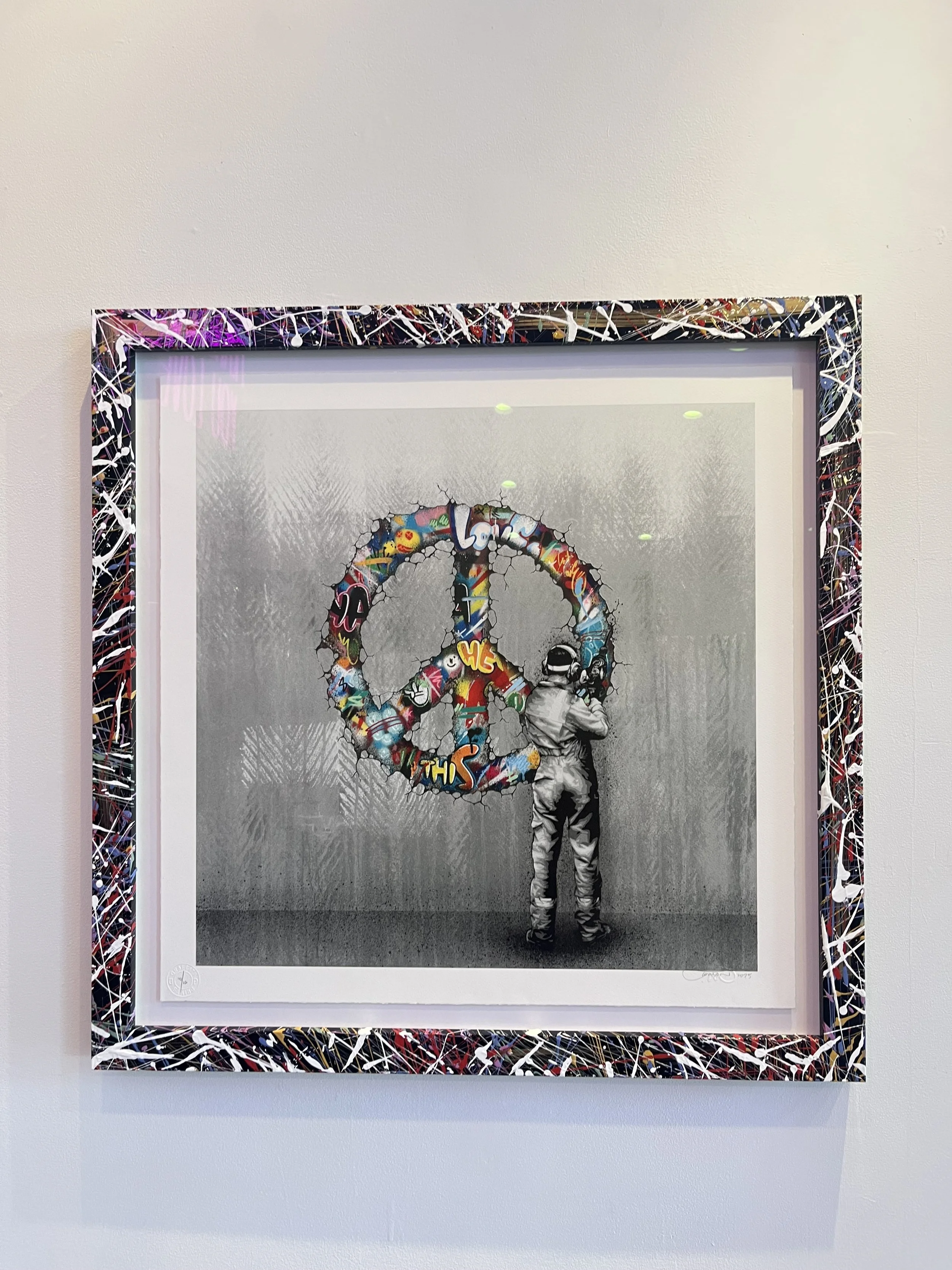 A graffiti-style artwork of a peace sign with colorful spray paint letters and words, a graffiti background, and a child wearing a hat standing in front, looking at the peace sign.