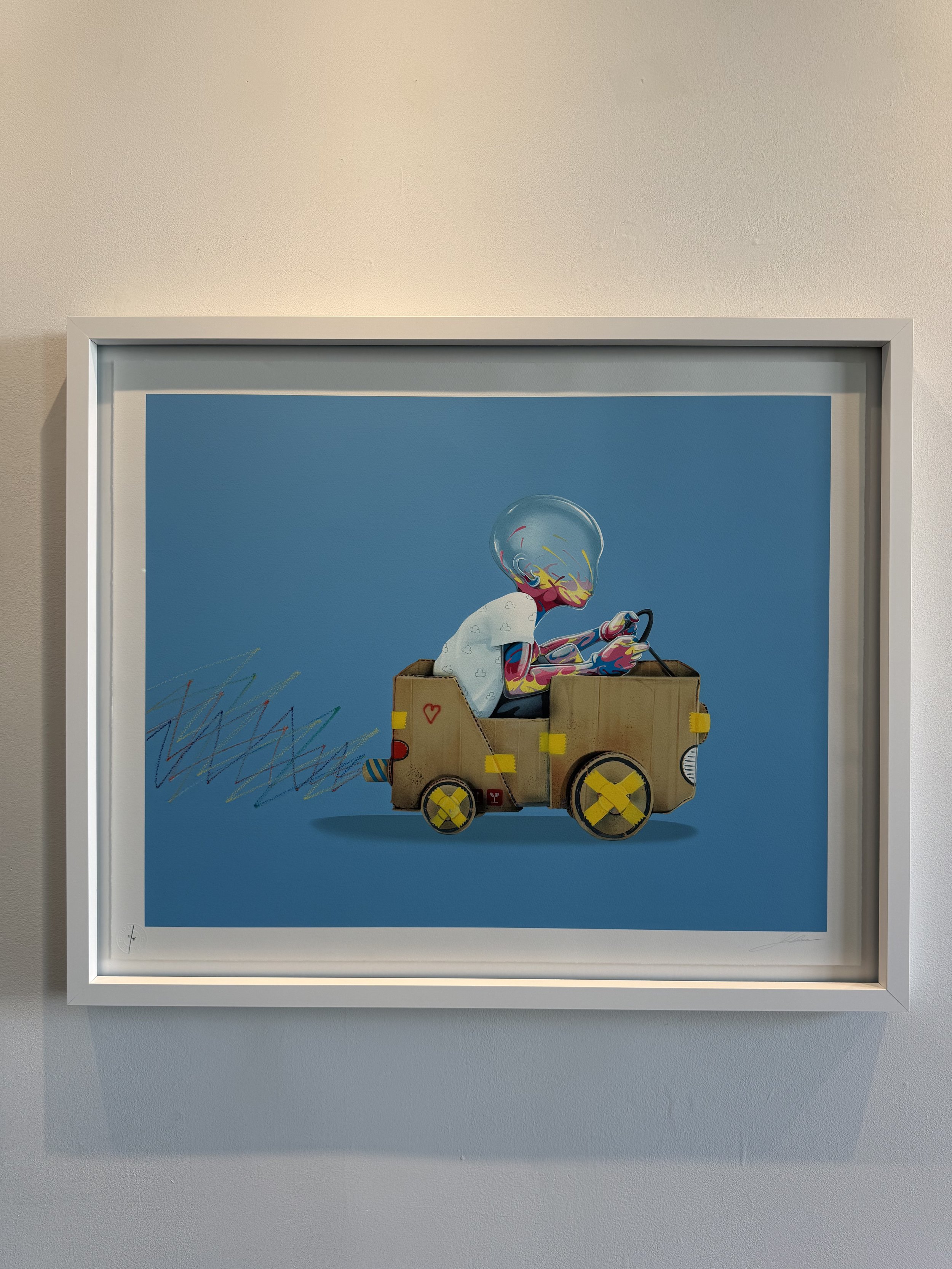 Artwork of a child-like figure with a transparent helmet, driving a cardboard box car with colorful scribbles and a trail of scribbles behind, set against a blue background.