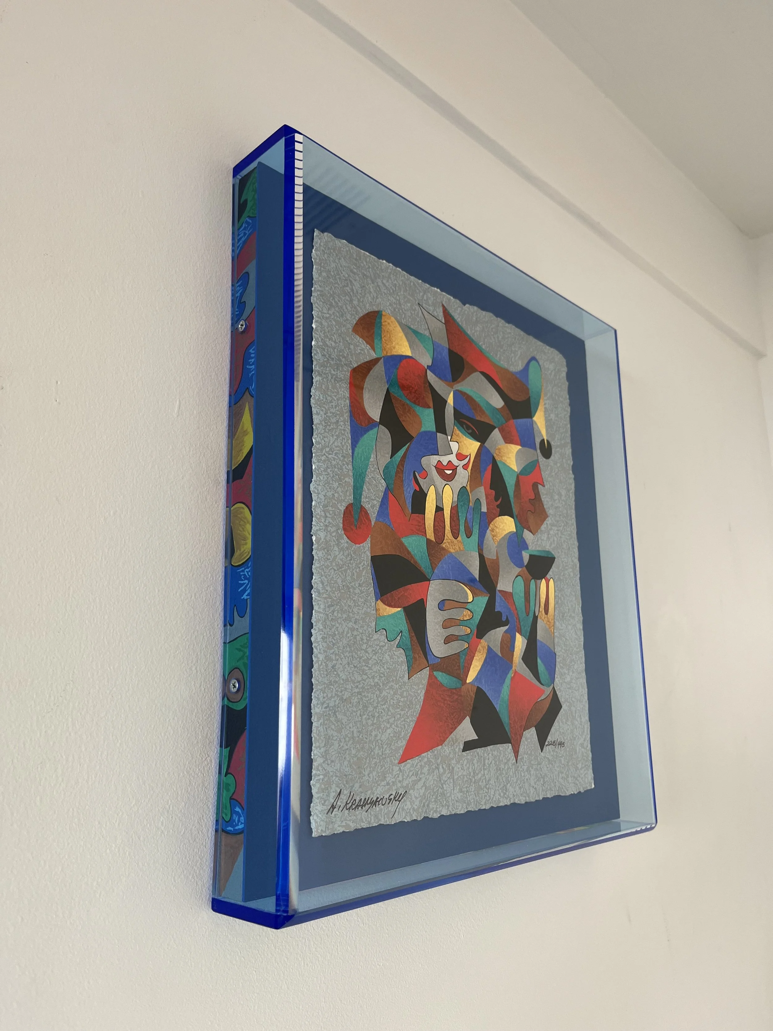 A colorful abstract mosaic artwork framed in a glass case, mounted on a white wall.