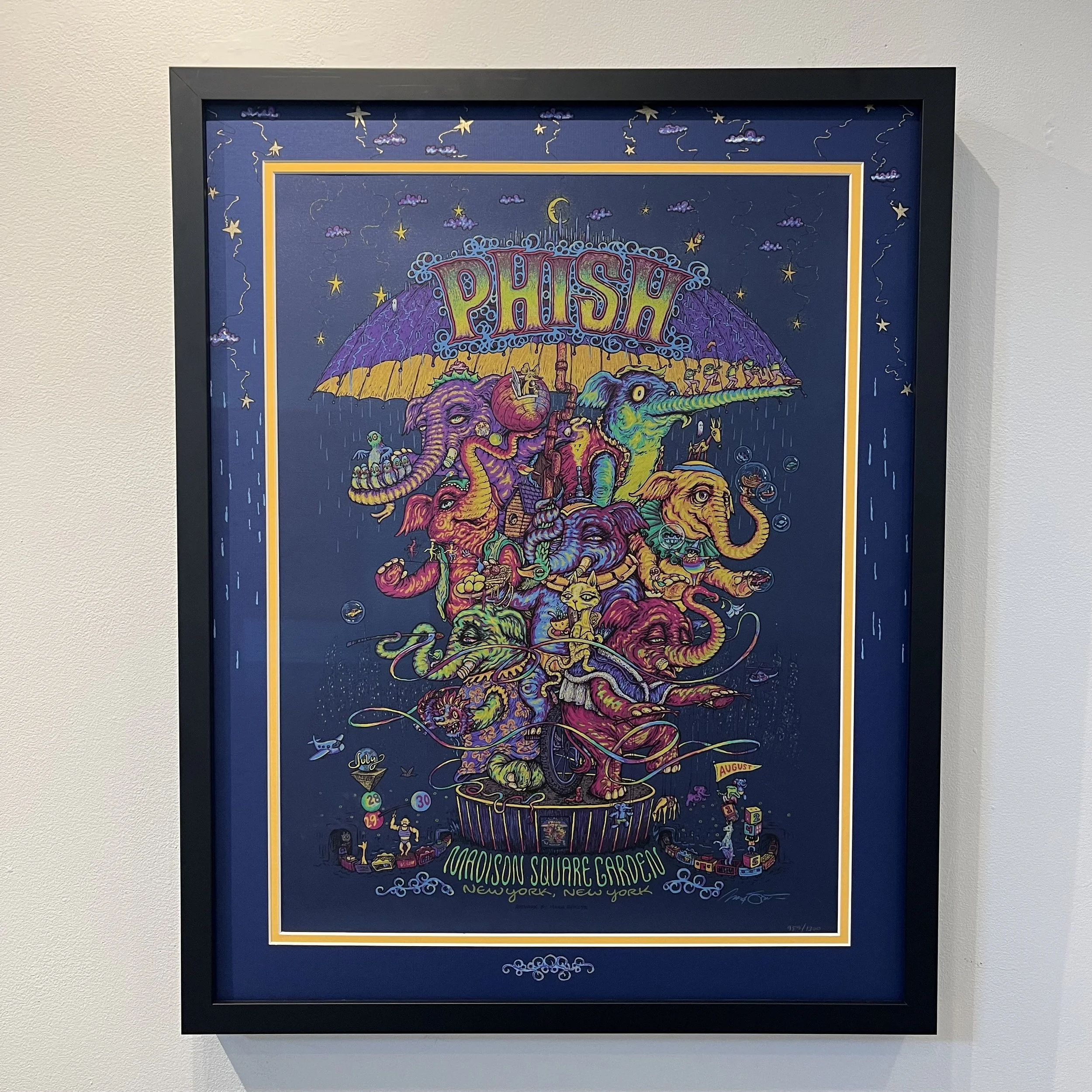 Colorful poster advertising a Phish concert at Madison Square Garden in New York, featuring whimsical, psychedelic illustrations of animals, rain, and a large umbrella with the band's name at the top.