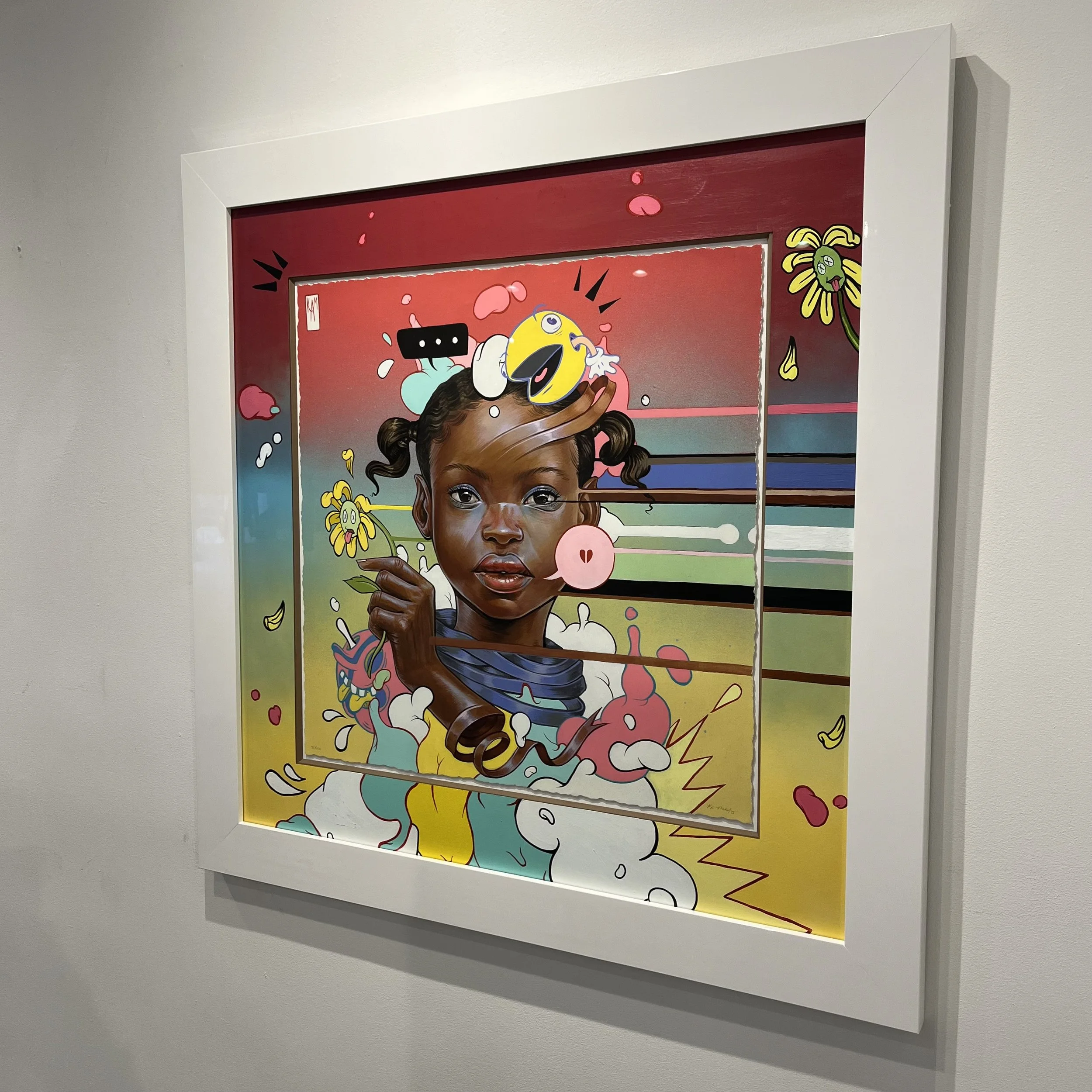 Colorful artwork of a young girl with a serious expression, surrounded by cartoonish and abstract elements, framed and hanging on a gallery wall.