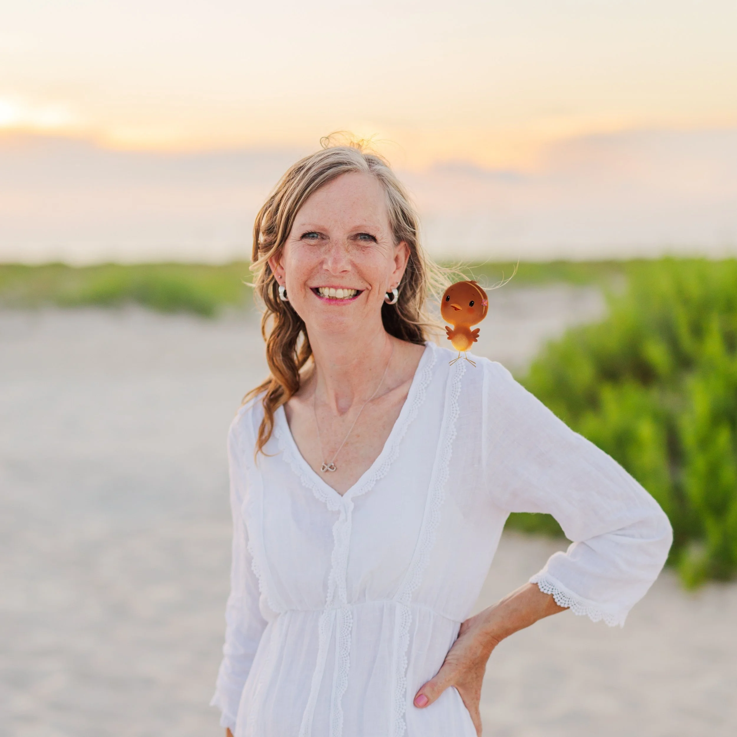 A smiling woman in a white dress standing outdoors on a beach at sunset, with a cartoonish orange chick perched on her shoulder.