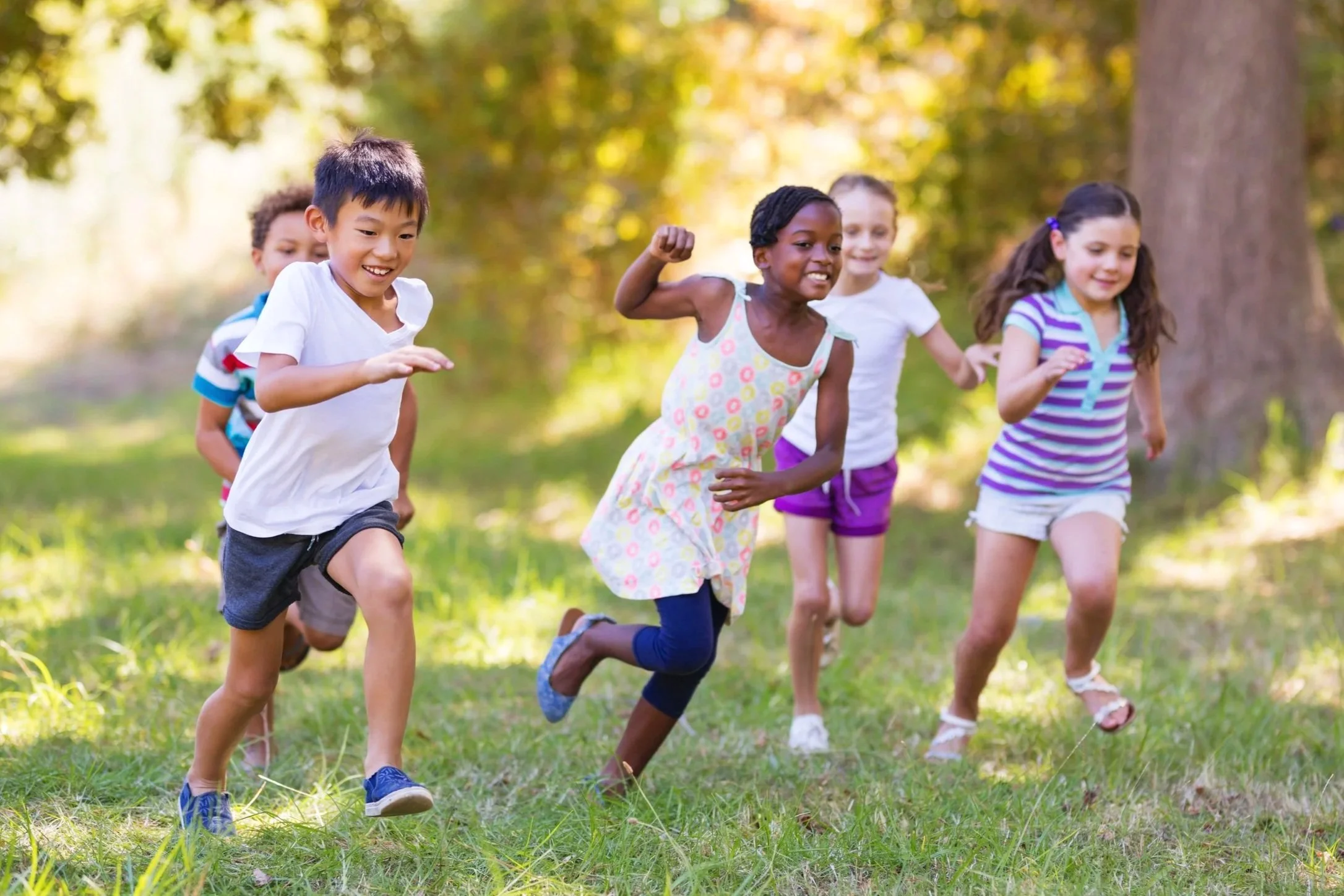 Group of children running outdoors in a park on a sunny day.