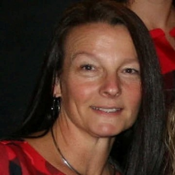 Close-up of a woman with long dark hair, wearing a red top, smiling slightly.