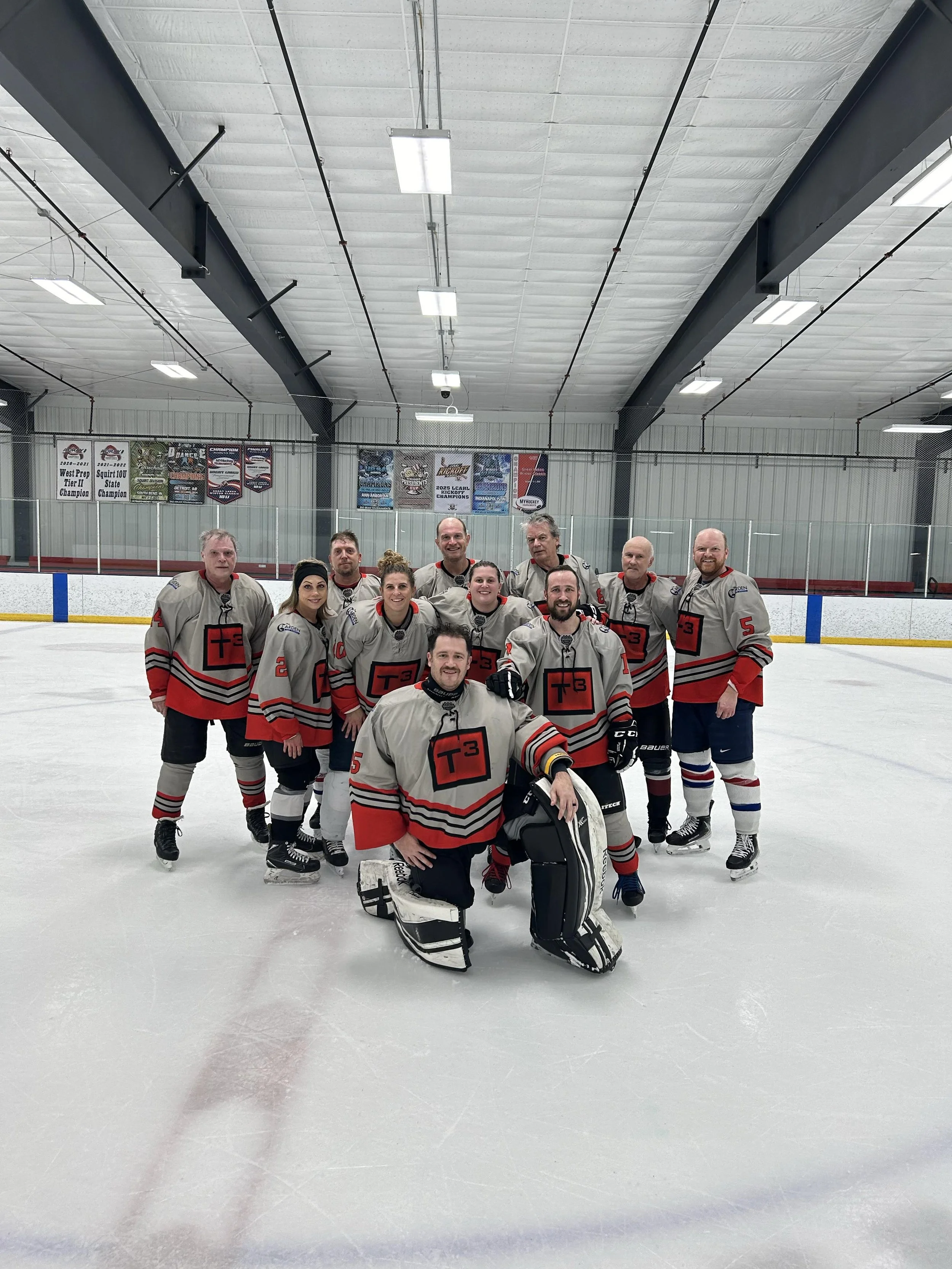 A group of hockey players on an ice rink, wearing gray and red jerseys, posing for a team photo.