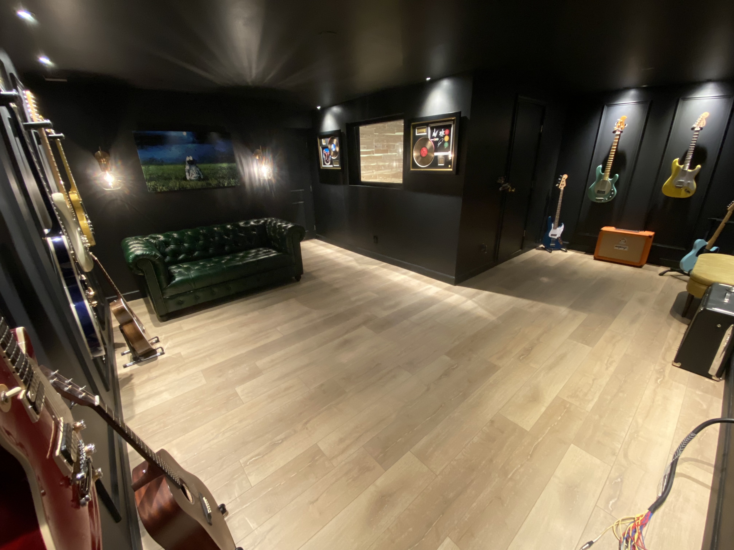 Music room with black walls, wooden floor, green leather couch, guitars displayed on walls, framed artwork, and guitar amplifiers.