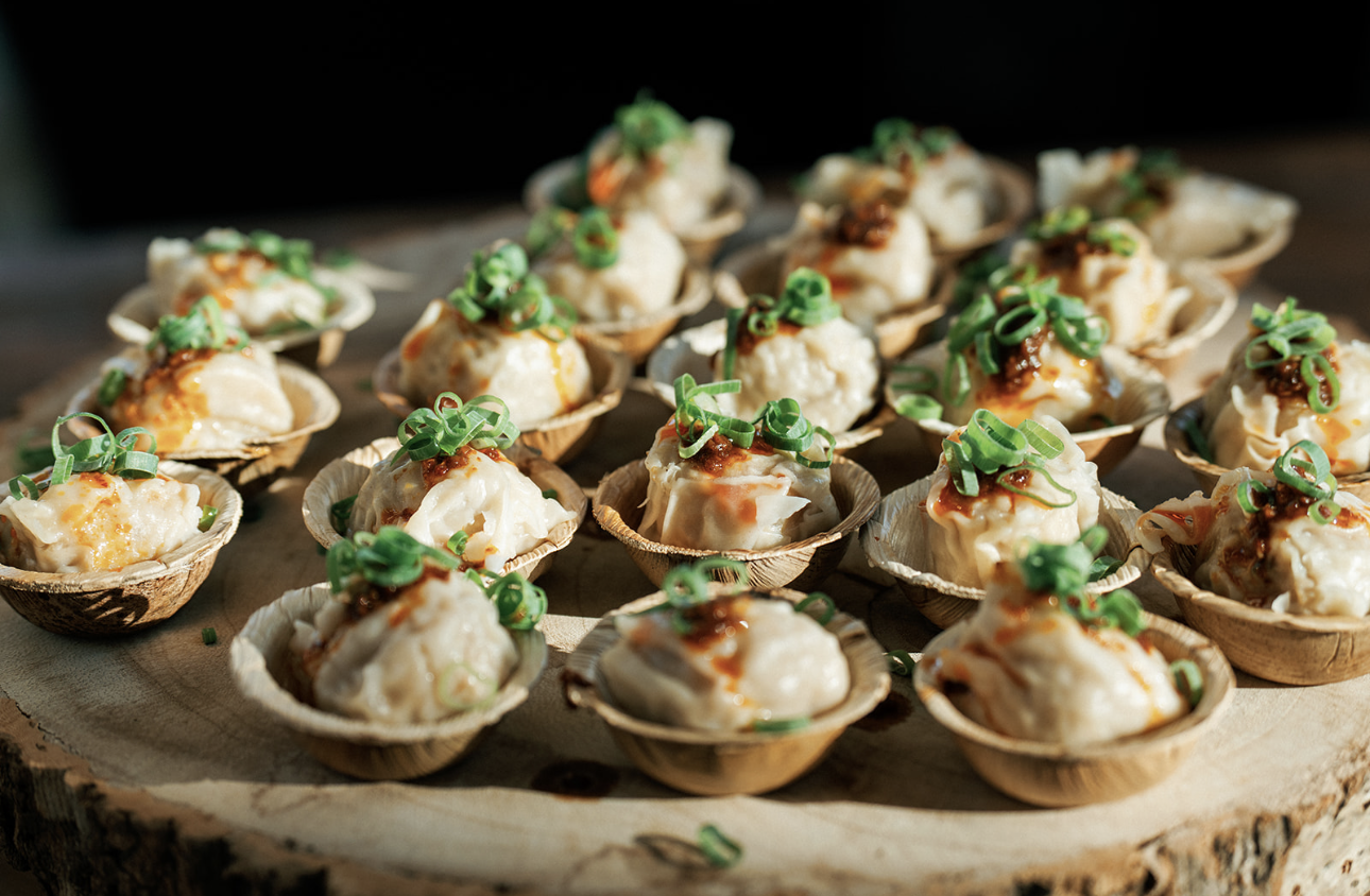 Several bite-sized appetizer balls garnished with green onions, served in small shell-shaped containers on a wooden board.