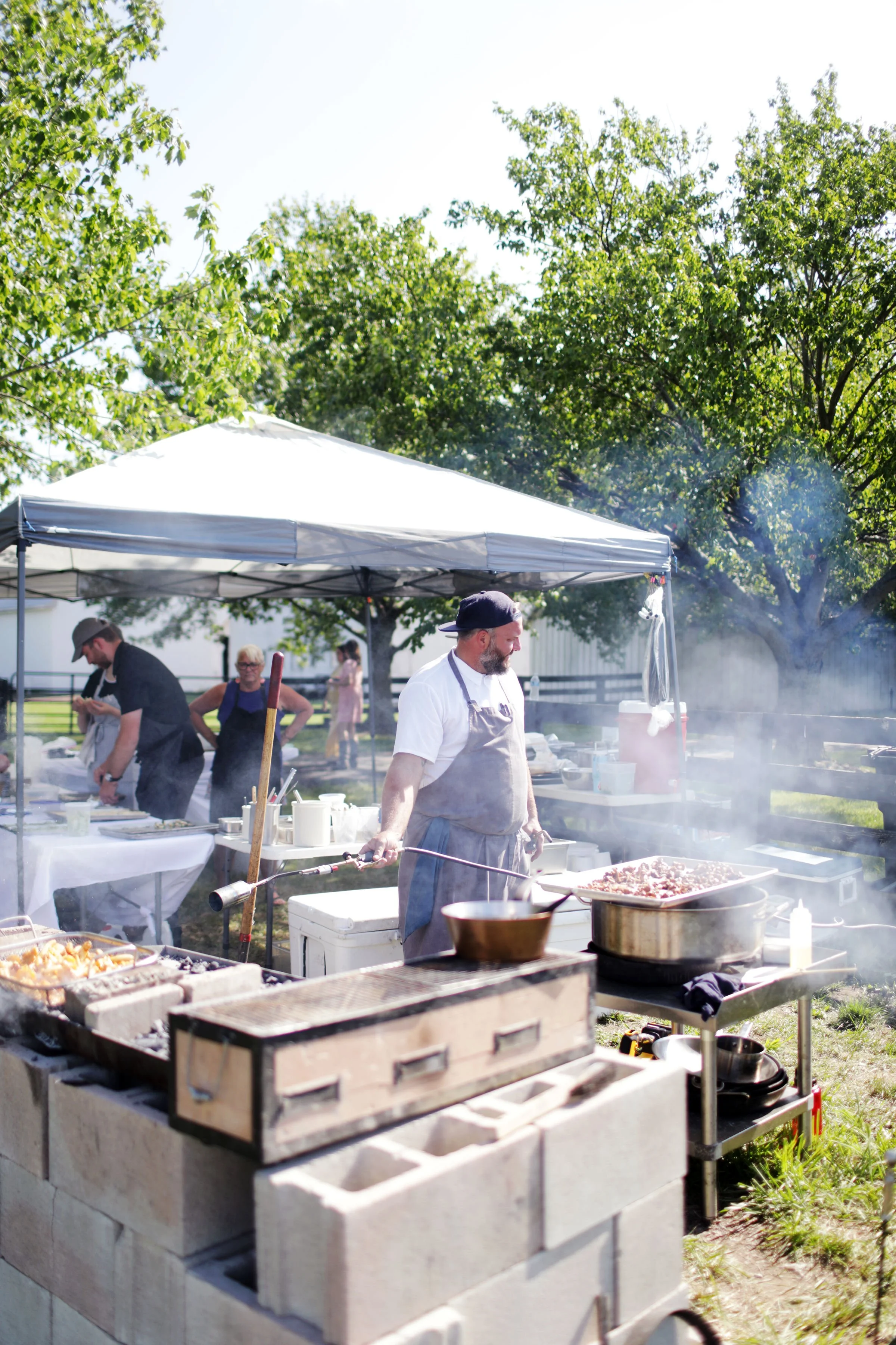 Chef Josh food under a canopy on a sunny day, with trees in the background.