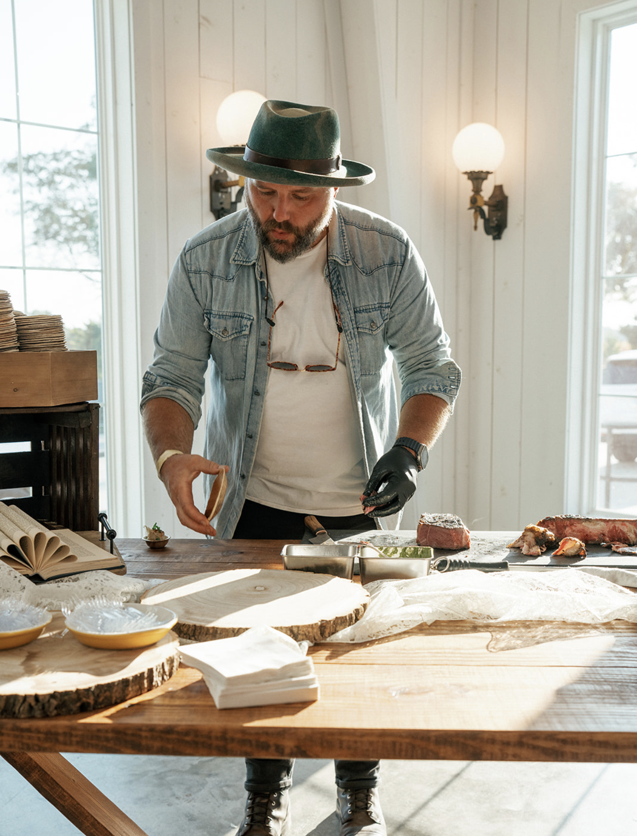 Chef Josh preparing meat in a bright kitchen with large windows.