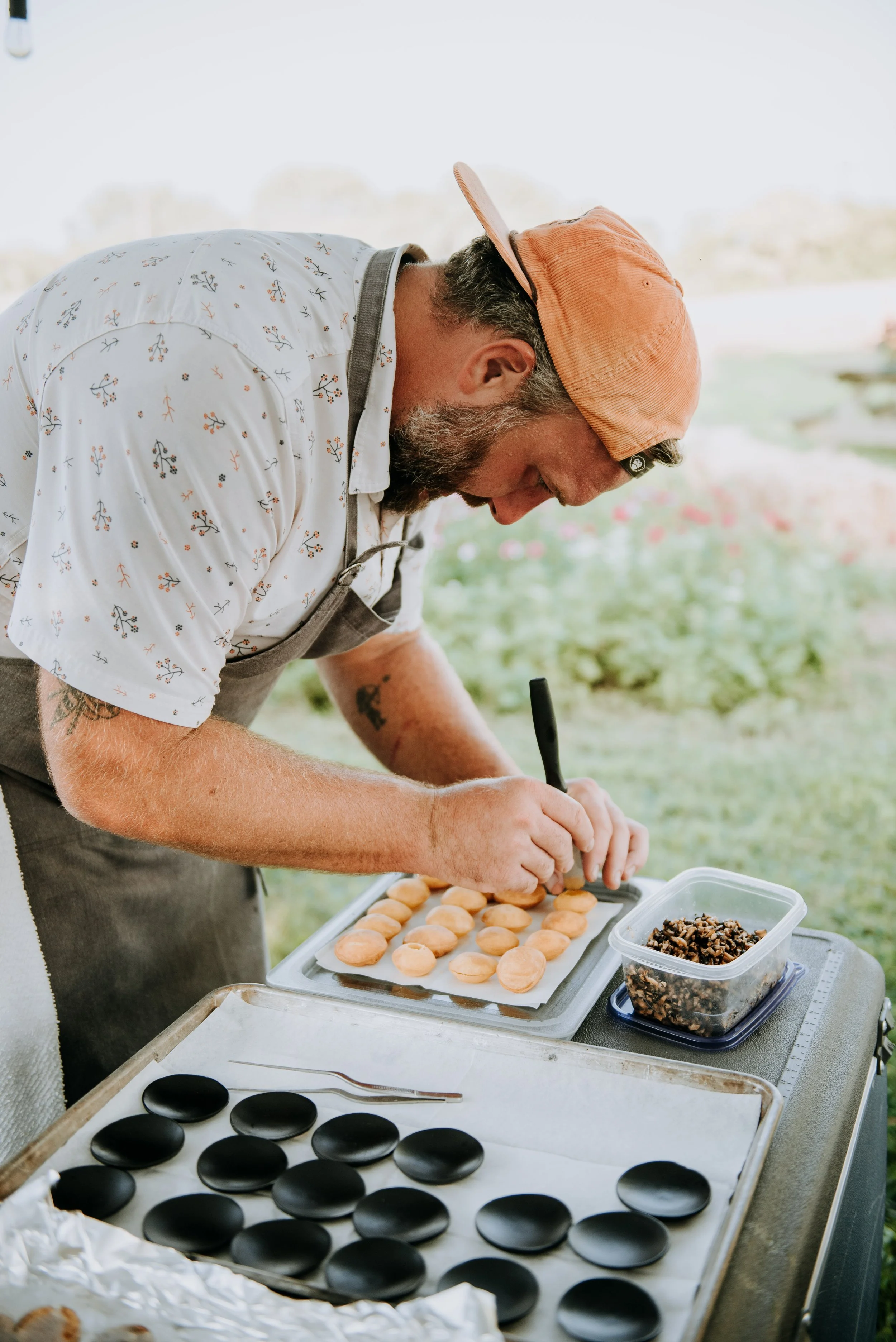 Chef Josh preparing food on a table outdoors, with black stones and a container of chopped ingredients.