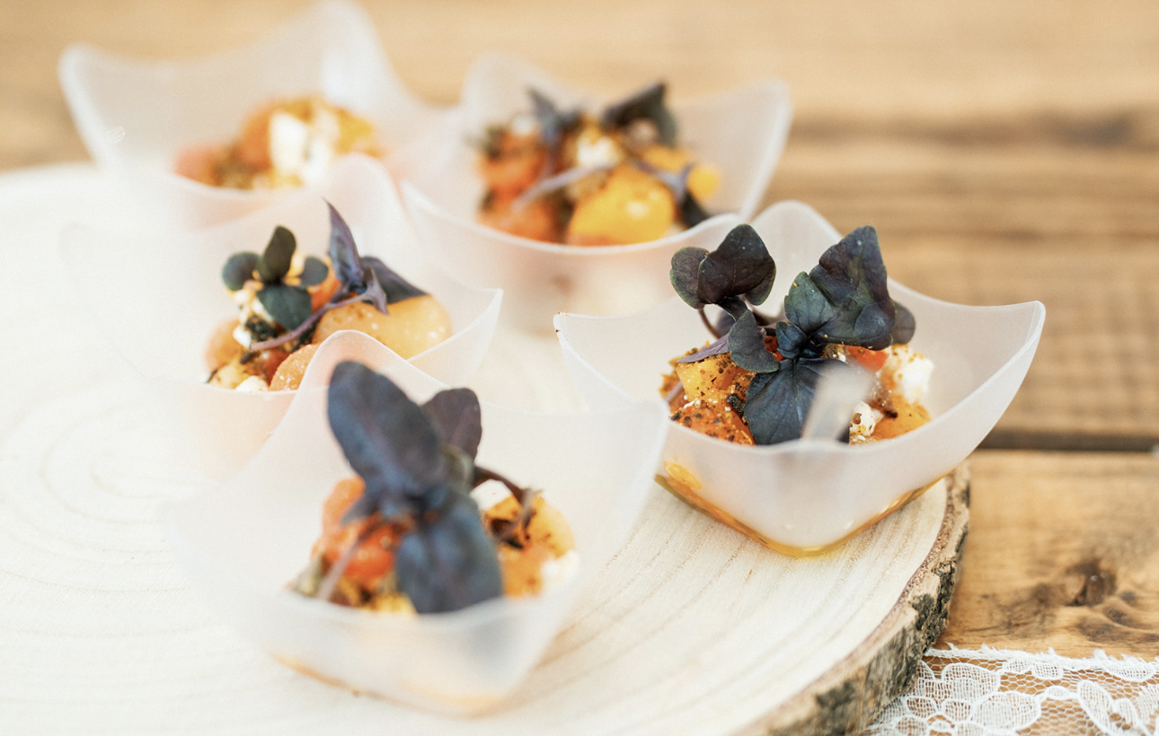Appetizers in white flower-shaped cups with black microgreens on a wooden serving board
