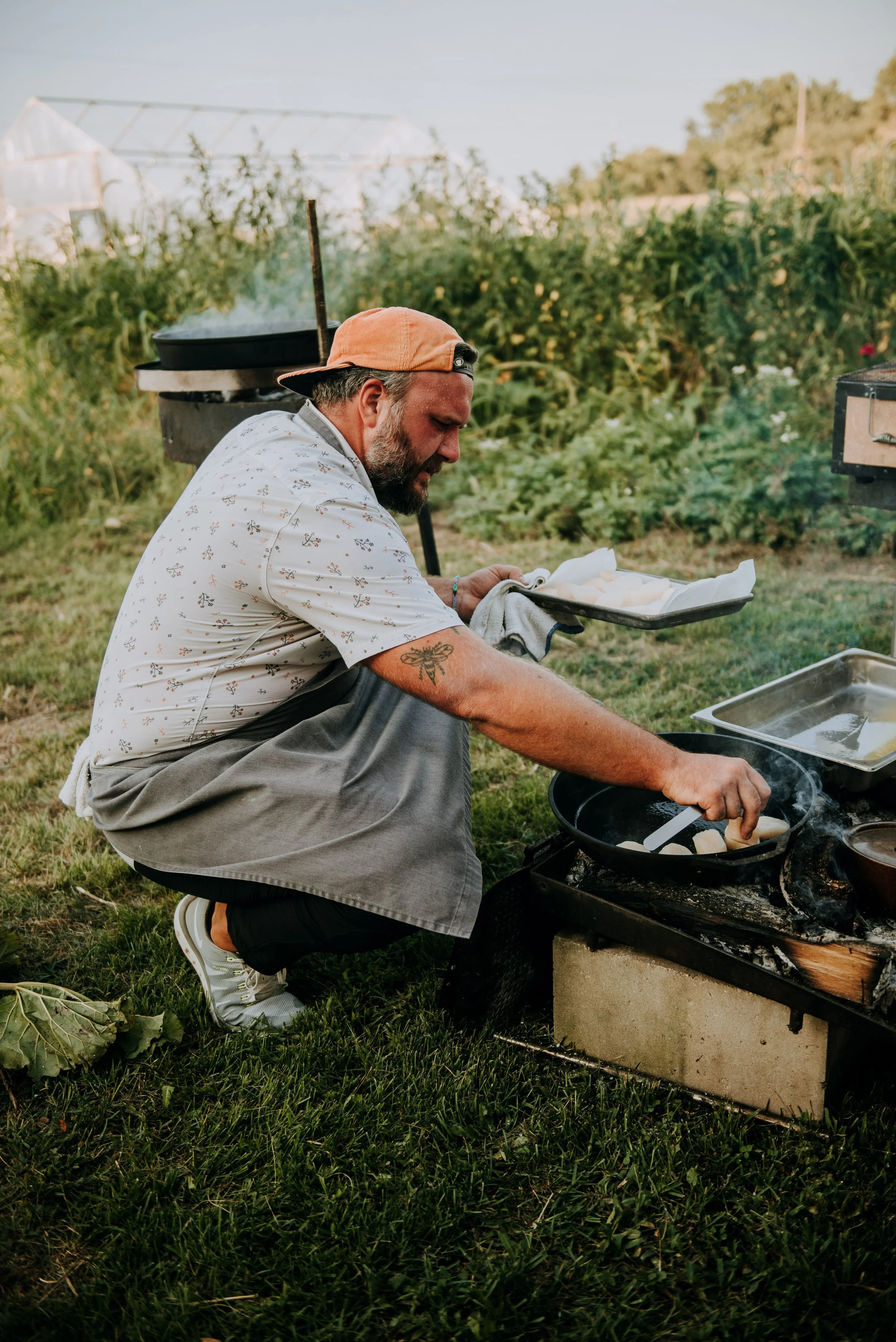 Chef Josh cooking outdoors on a portable stove in a garden or farm with greenery and plants in the background.