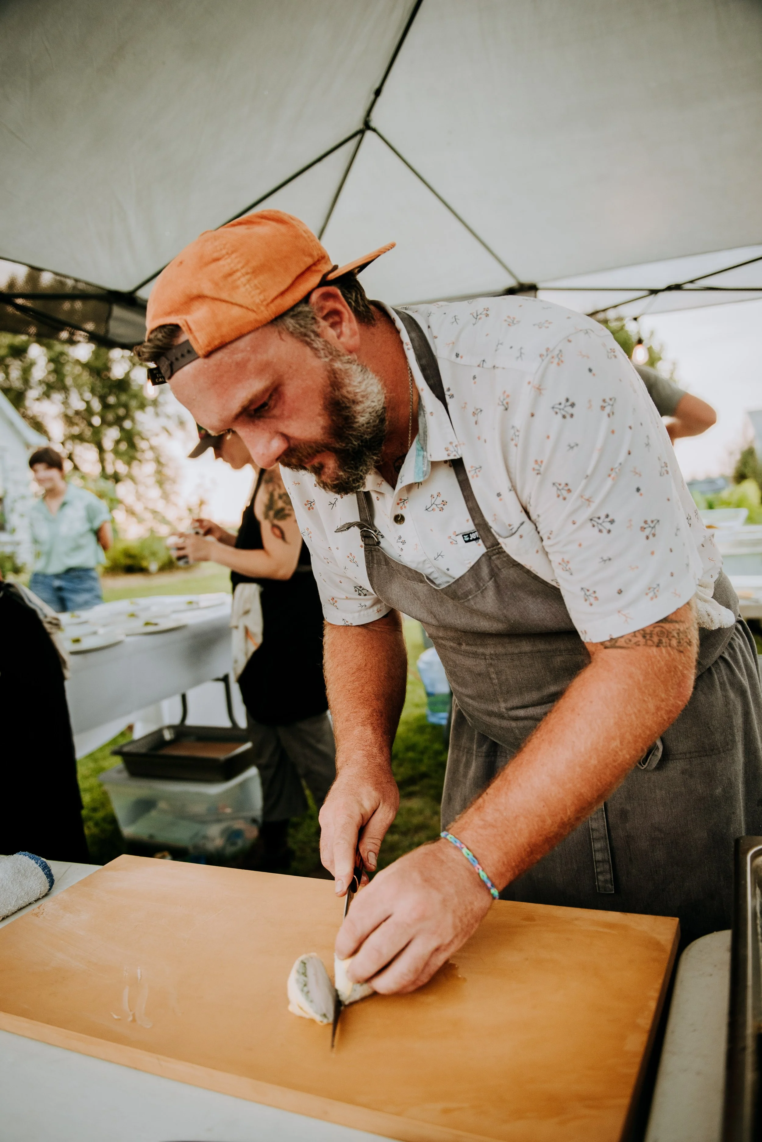 Chef Josh prepping fish on a wooden cutting board under a tent at an outdoor event.