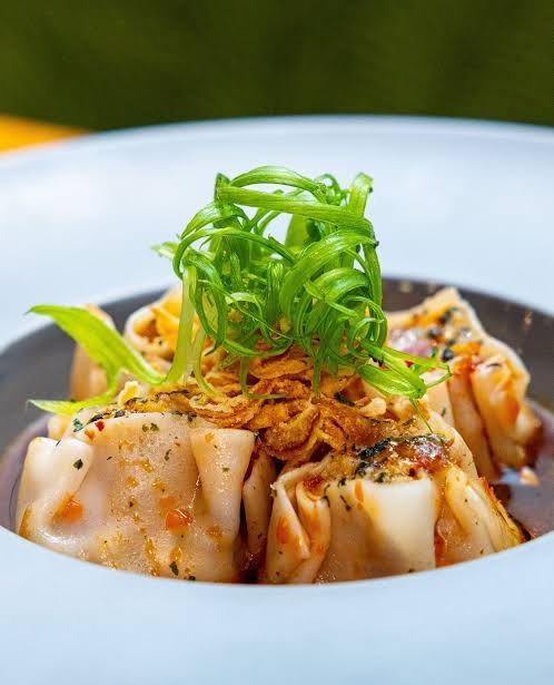 Steamed dumplings garnished with chopped green onions, served with a dipping sauce.