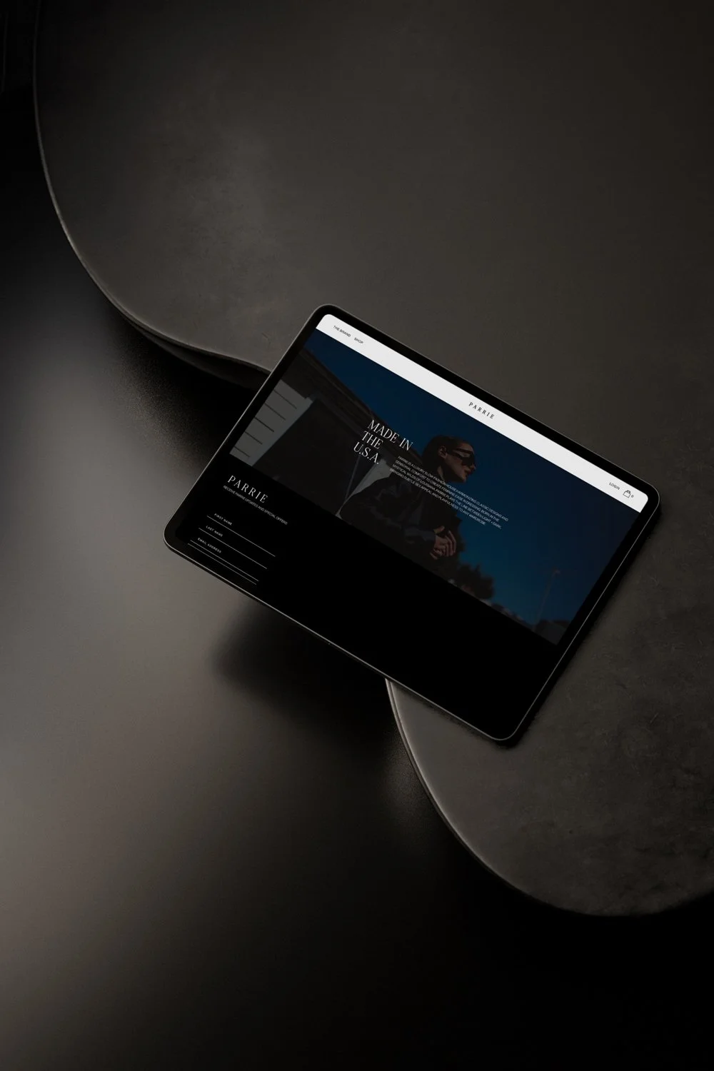 A tablet placed on a dark, curved surface displaying a website with a woman wearing sunglasses against a blue sky background.