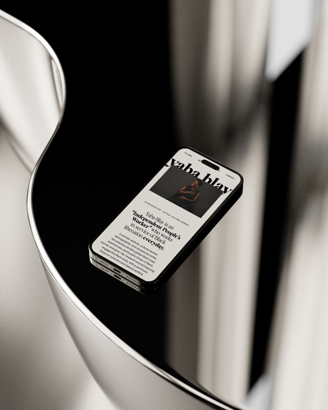 Smartphone with website displaying a person and text, resting on a black shiny surface near a metallic vertical structure.