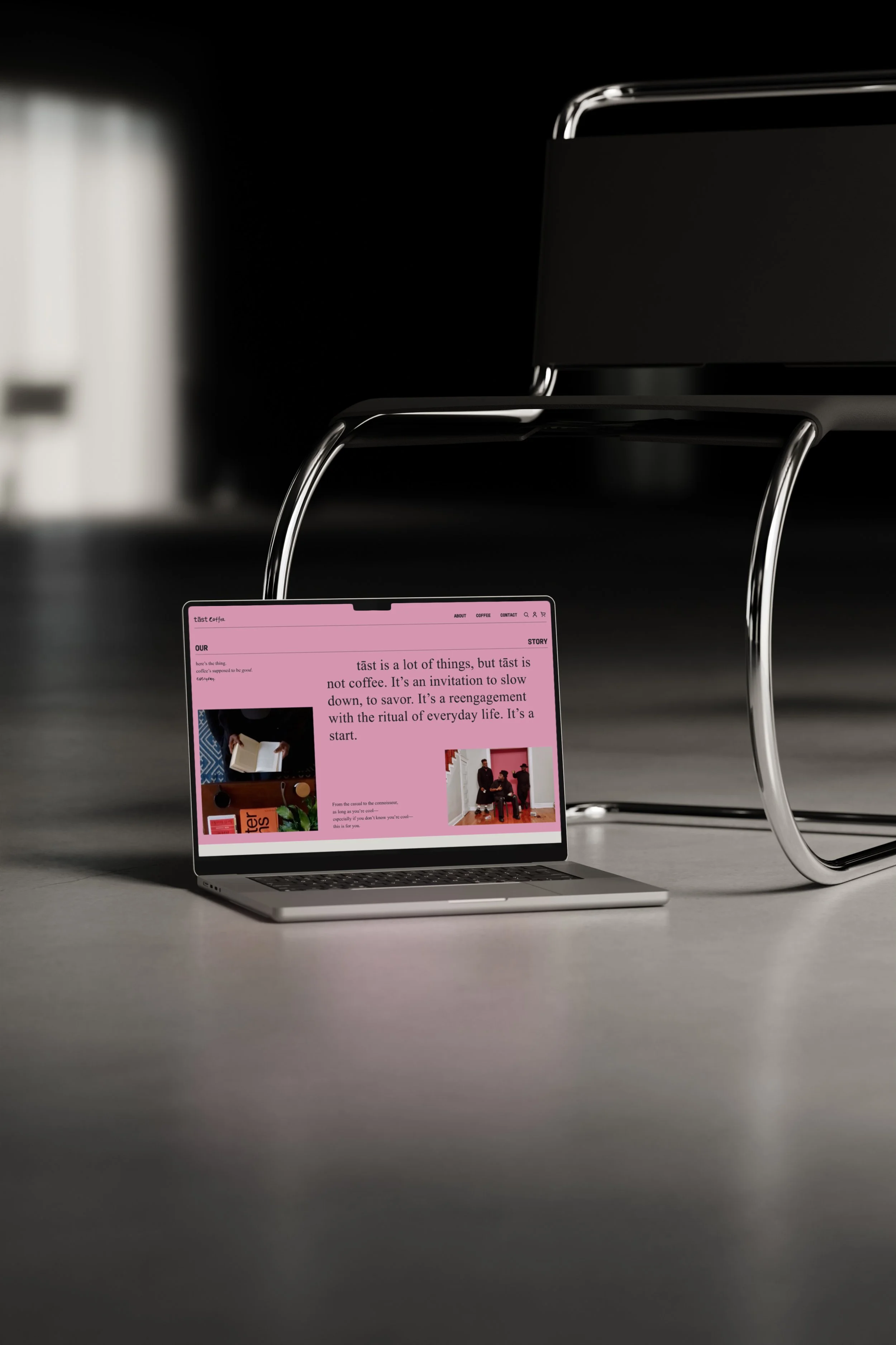 A laptop with a pink webpage open, placed on a gray floor in front of a black chair with chrome legs in a minimalistic, modern setting.