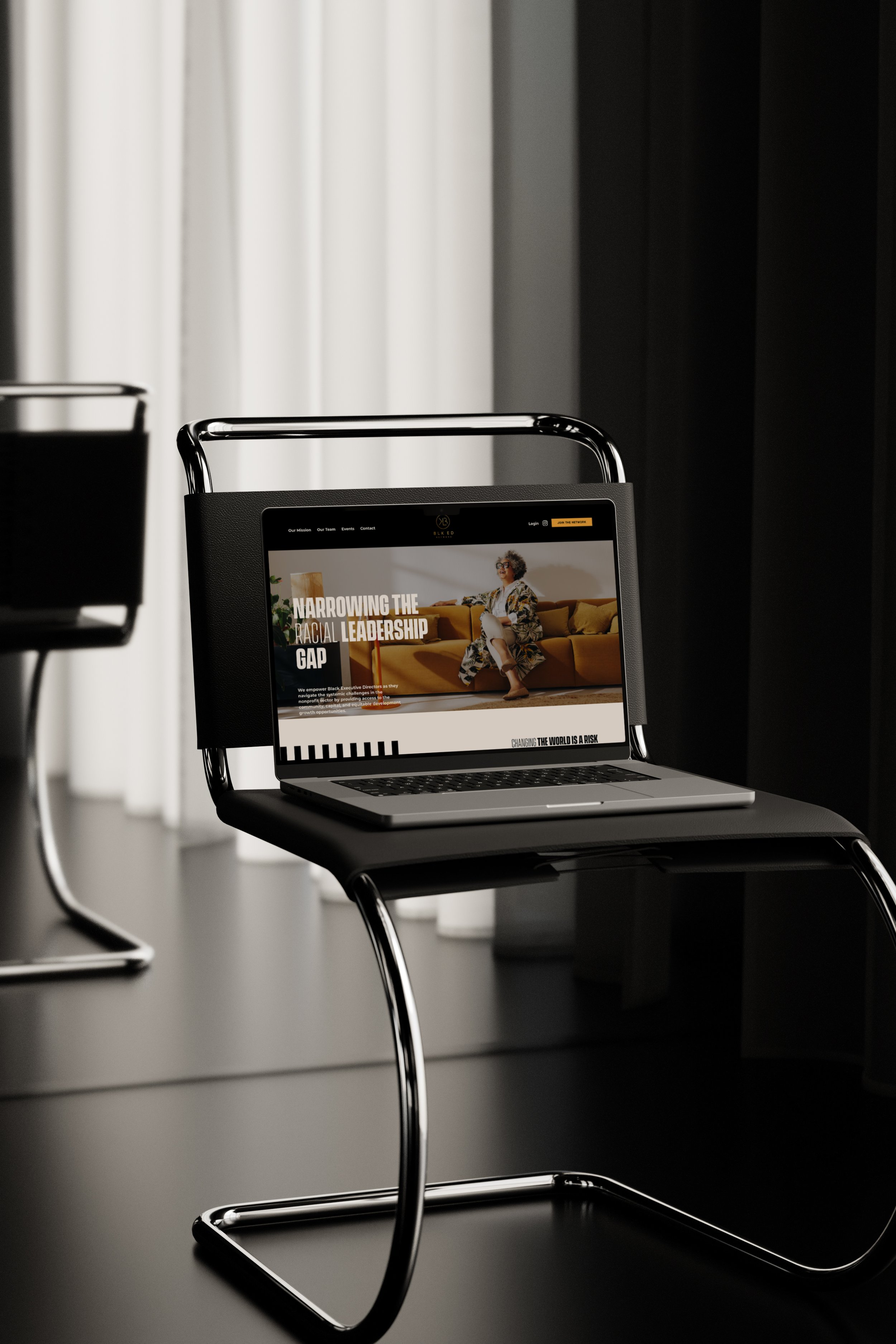 A laptop on a black chair in a modern office space with white and black curtains in the background.