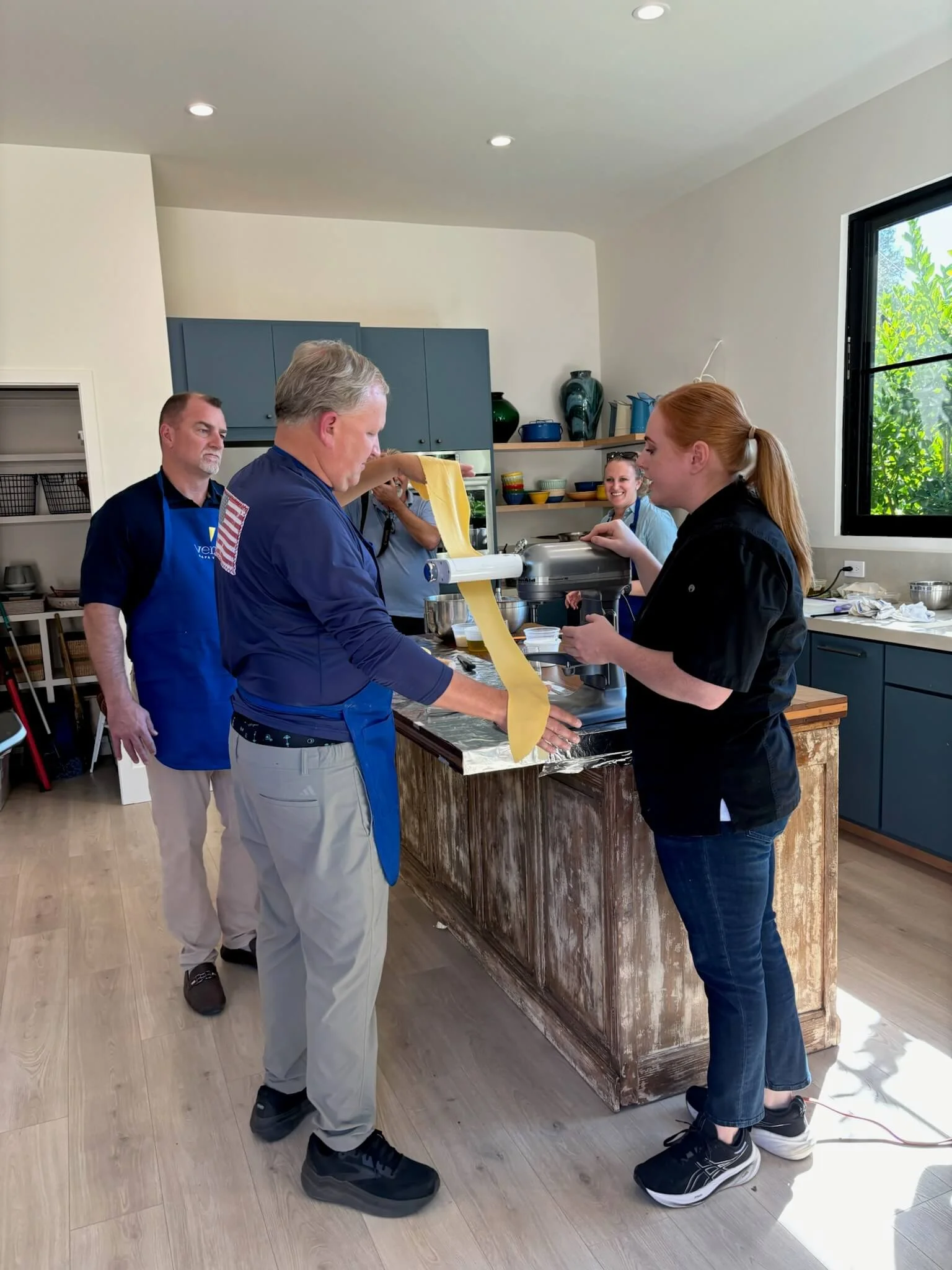 People making fresh pasta dough in a kitchen with blue cabinets and open shelves.