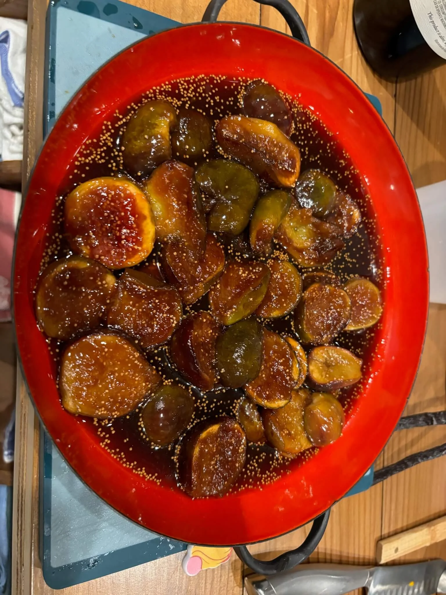 A red bowl filled with ripe figs soaked in syrup, garnished with sesame seeds.