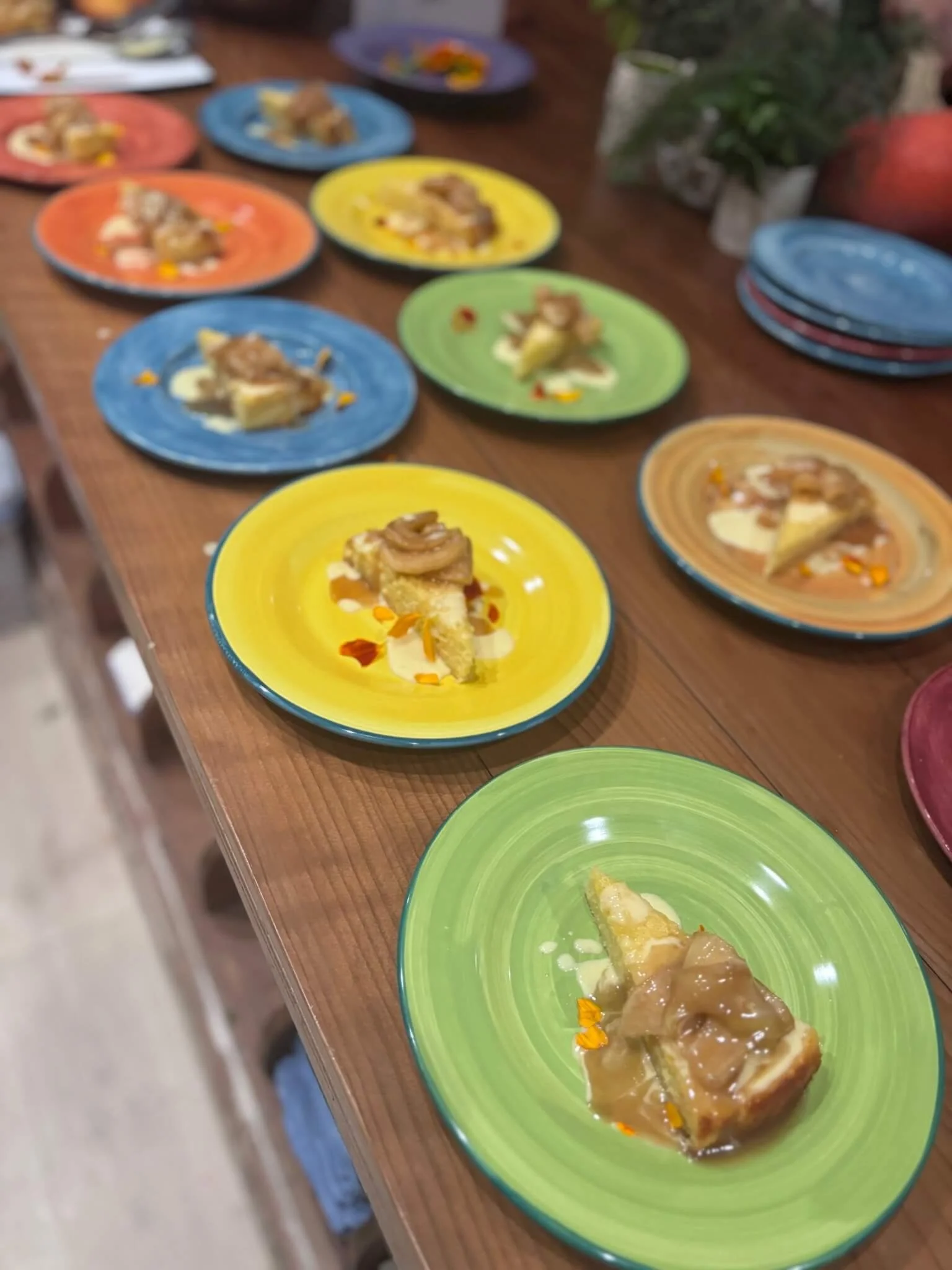 Colorful plates with dessert slices topped with caramel and garnished with orange flower petals arranged on a wooden table.