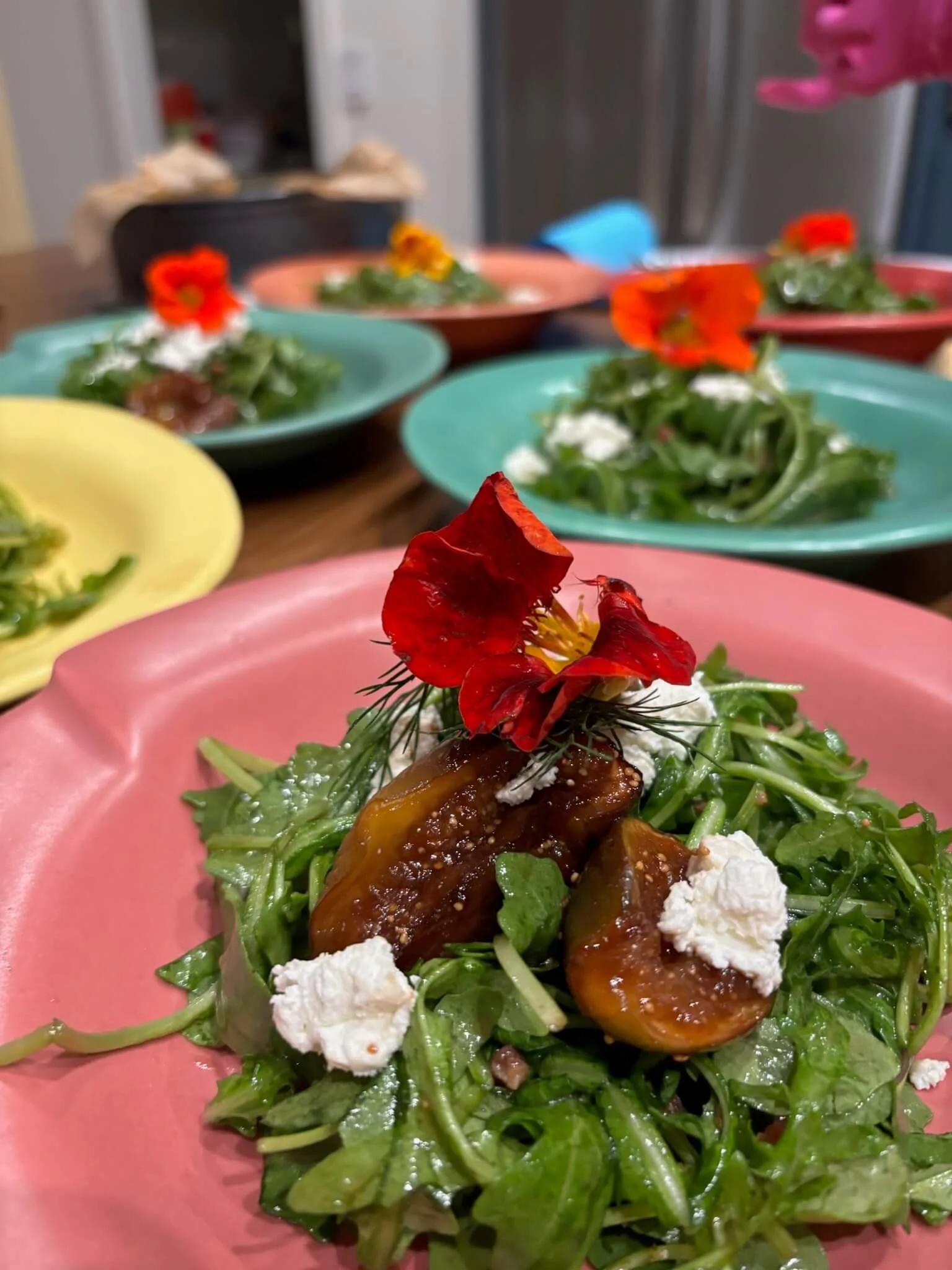 Colorful plates of salad with greens, cheese, and edible flowers on a table.