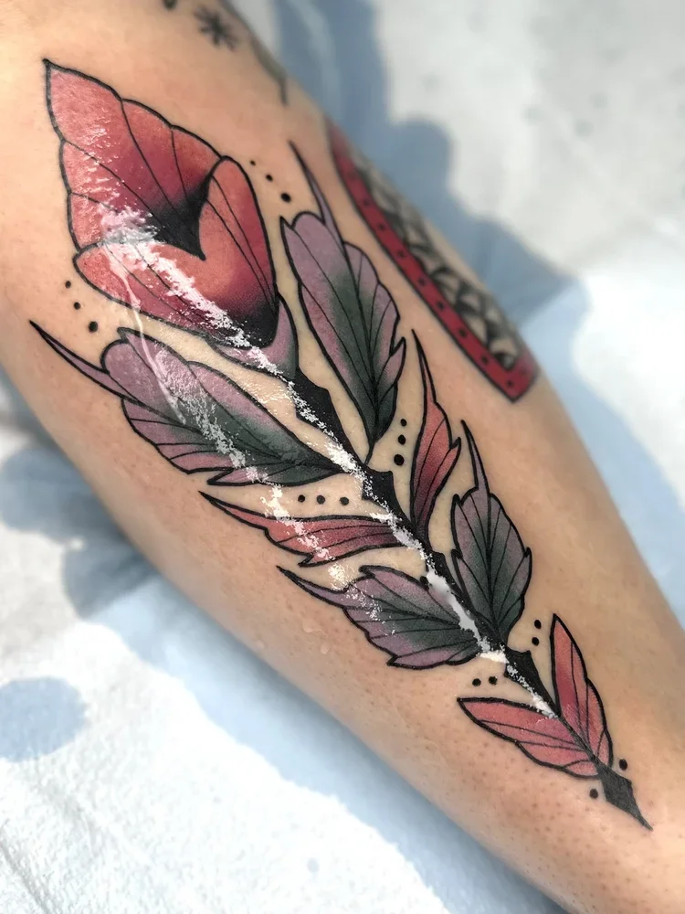 A colorful tattoo of a butterfly and leaves on a person's arm, with black outlines and pink, purple, and green shades.