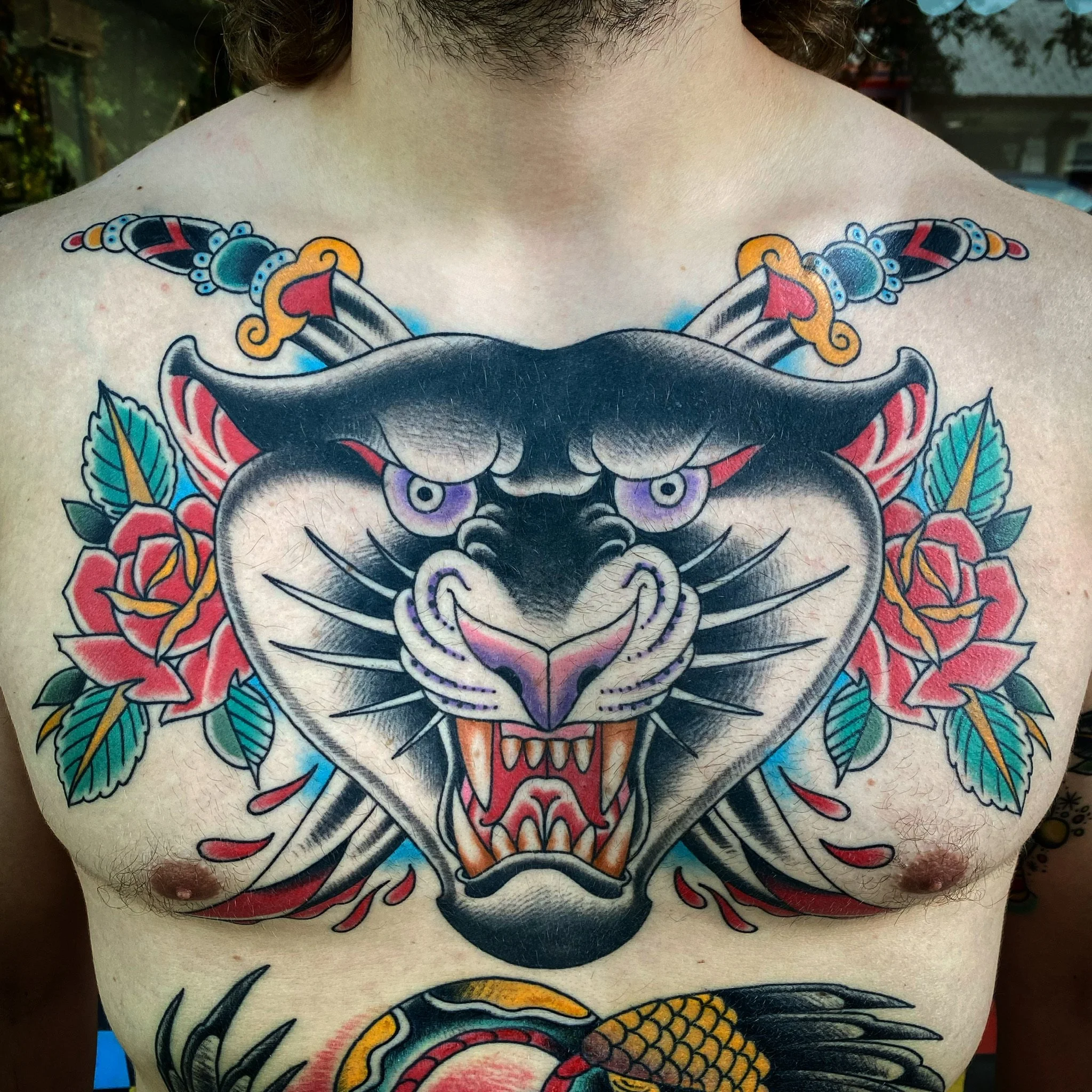Tattoo of a fierce black and white tiger's face with purple eyes, surrounded by red roses and green leaves, on a person's chest.