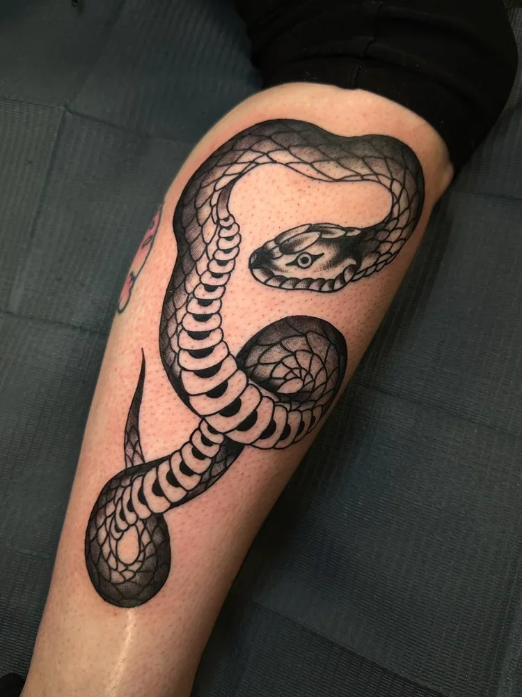 Black and gray tattoo of a coiled snake on a person's leg.