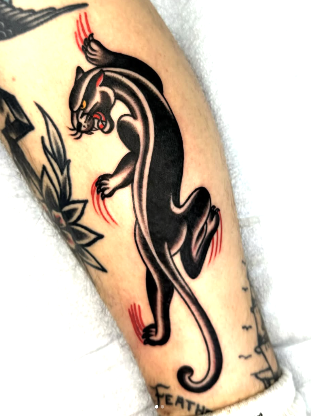 Traditional-style tattoo of a black panther with yellow eyes, accompanied by some green leaves, on a person's arm.