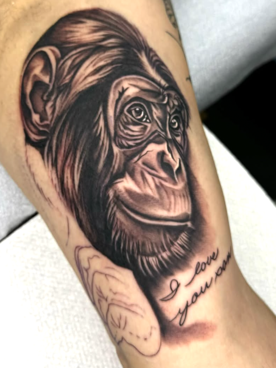 Black and gray tattoo of a realistic gorilla's face with a heartfelt quote 'I love you more' below it on person's arm.