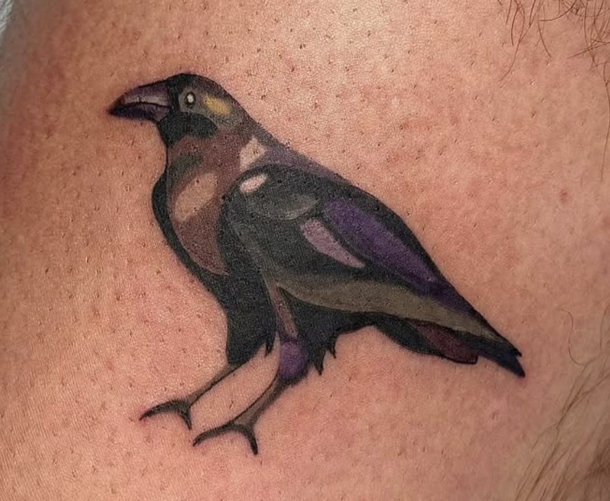 A colorful bird tattoo featuring shades of black, purple, and brown on the person's skin.