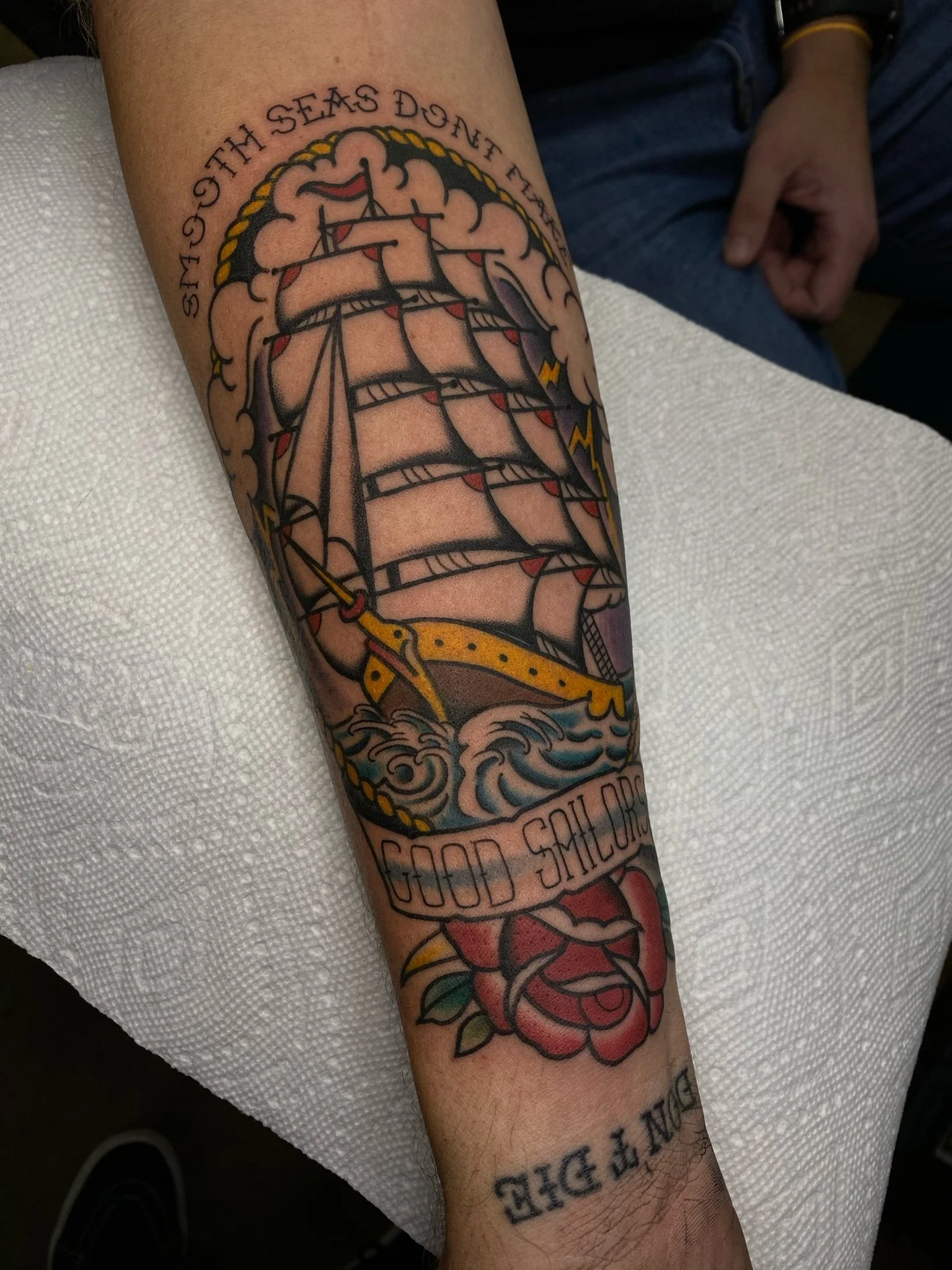 Tattoo of a sailing ship on waves with the phrase "Sail These Seas Don't F*** With Me" above the ship and "Good Sailor" below, and a rose at the bottom.