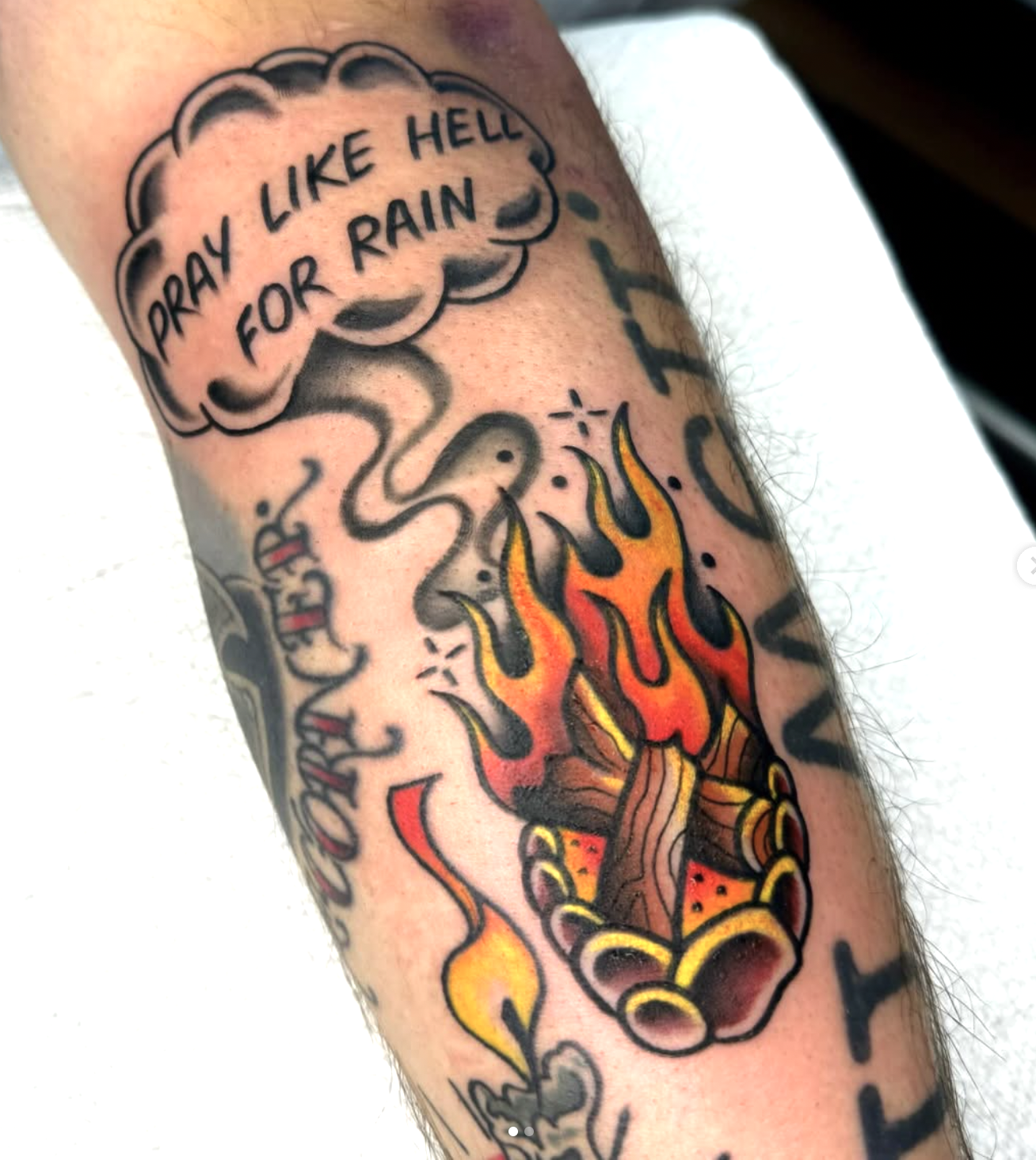 Tattoo of a flaming torch with a smoky cloud above it containing the words "Pray Like Hell For Rain."