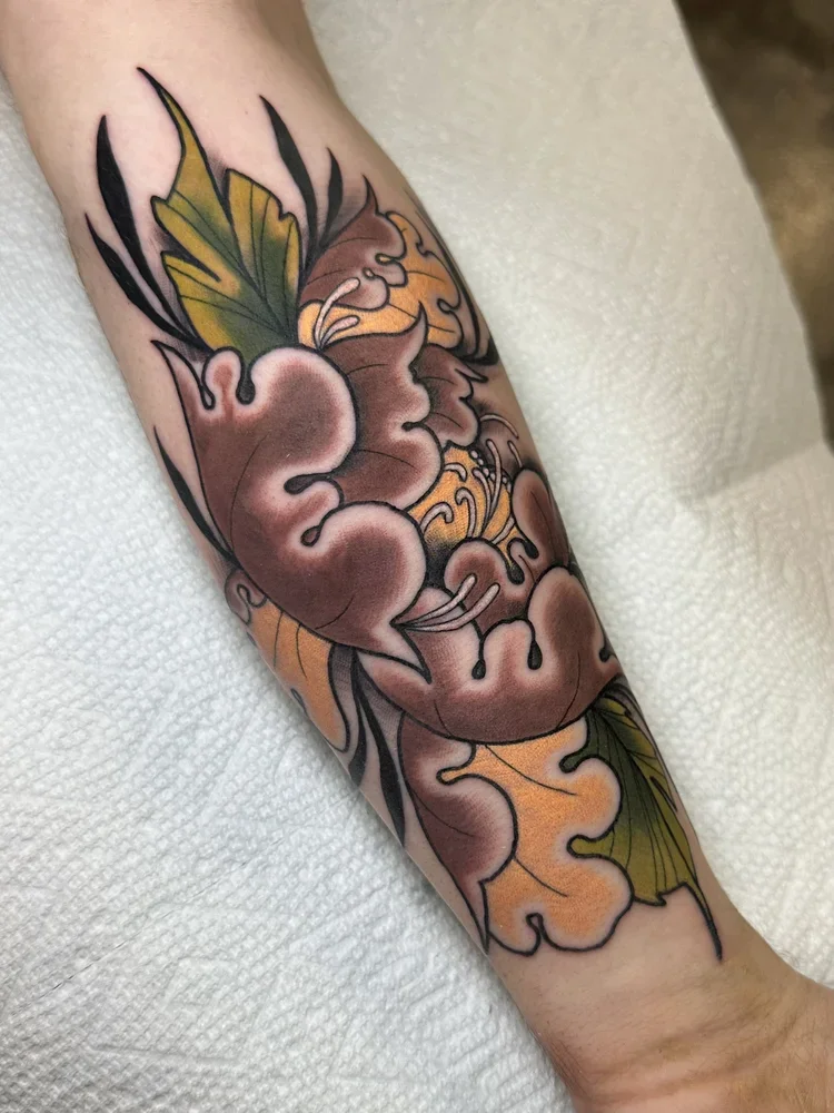 Colorful tattoo of a stylized heart with swirling lines, accompanied by green and yellow leaves.