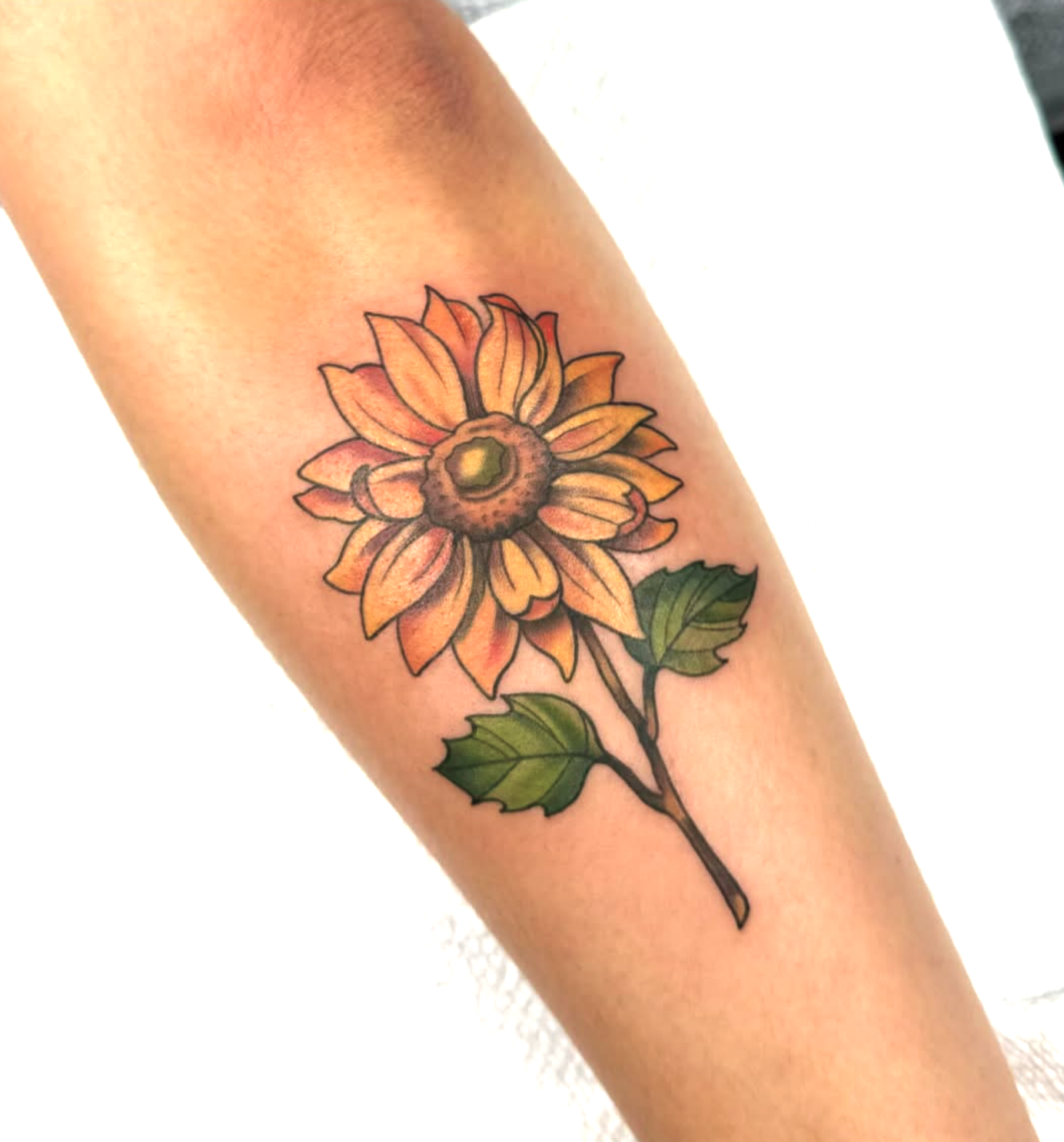 Colorful sunflower tattoo on person's arm with green leaves.