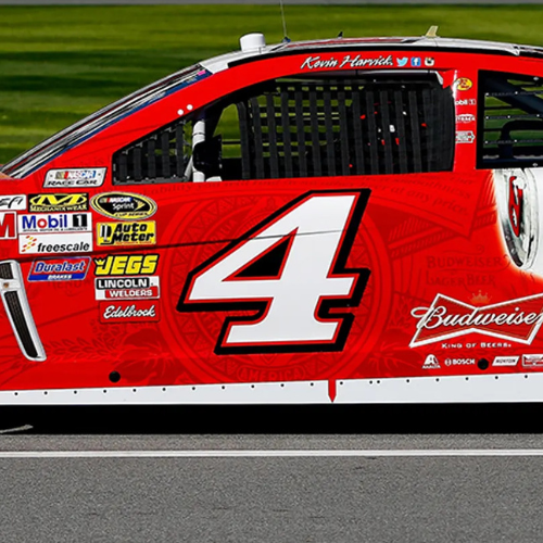 Close-up of a red race car with a large white number 4 on the side. Various sponsor logos are visible, including Budweiser, AutoMeter, WEG'S, Lincoln Welders, and Bosch. The name Kevin Harvick is written above the window.