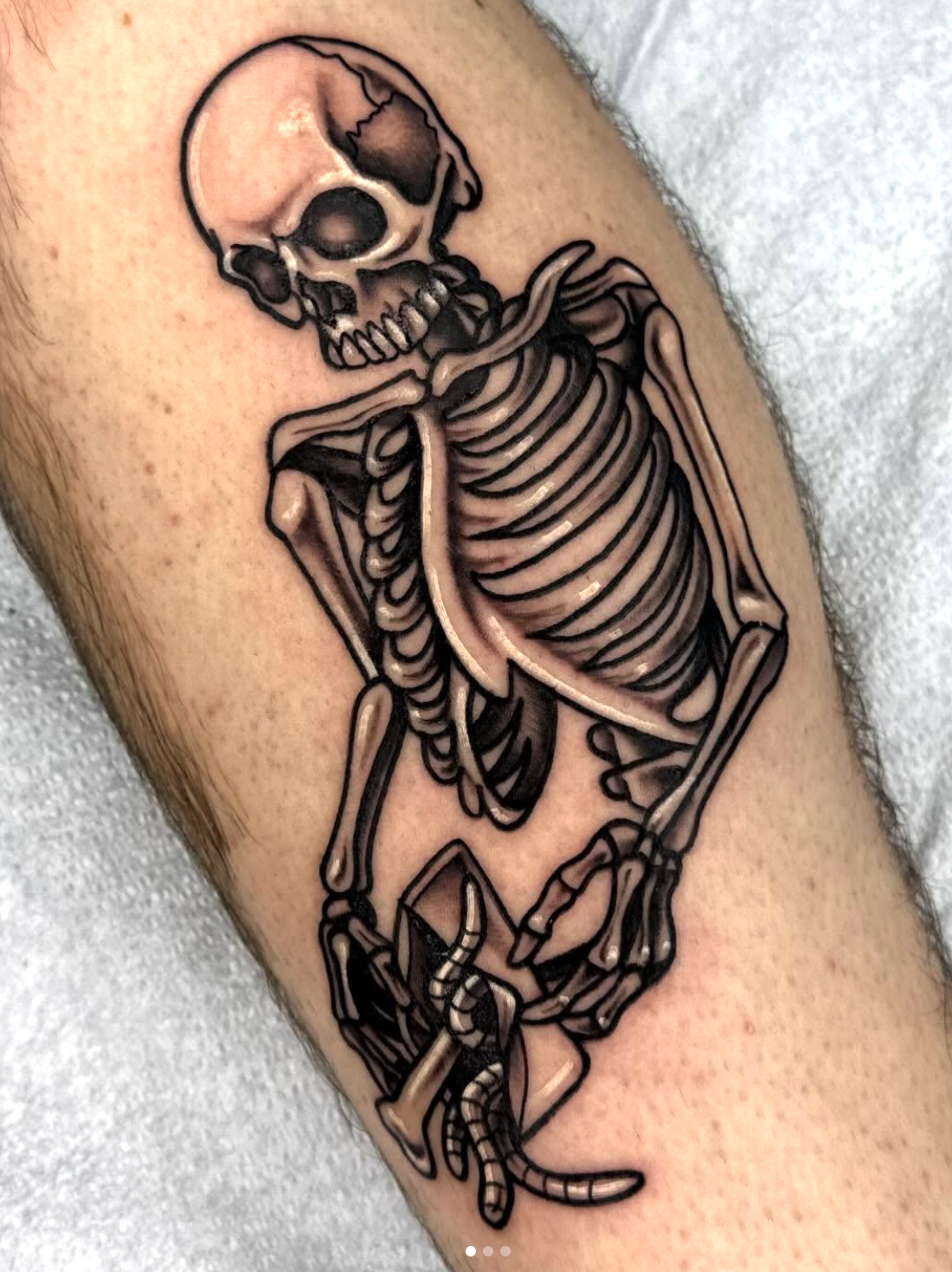 Tattoo of a human skeleton holding a drill on the arm.
