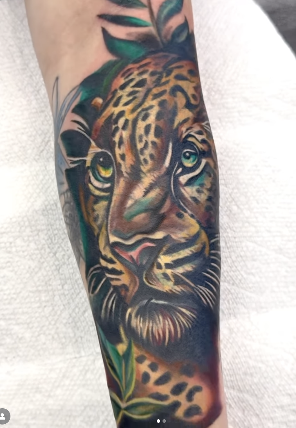 Colorful tattoo of a leopard's face on a person's arm, with green leaves surrounding it.