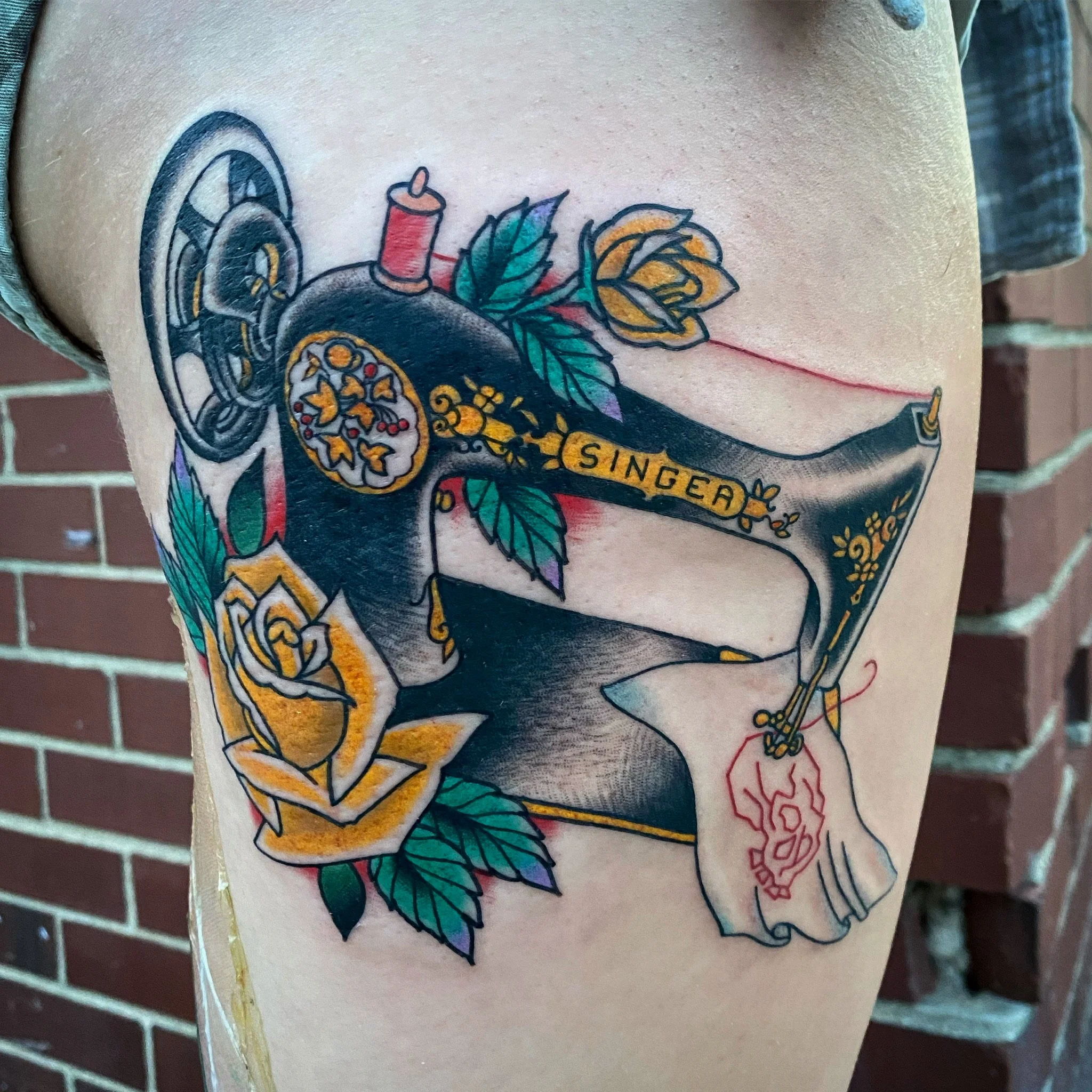 Tattoo of a vintage Singer sewing machine with roses and leaves, and the word "SINGER" on the machine's arm.