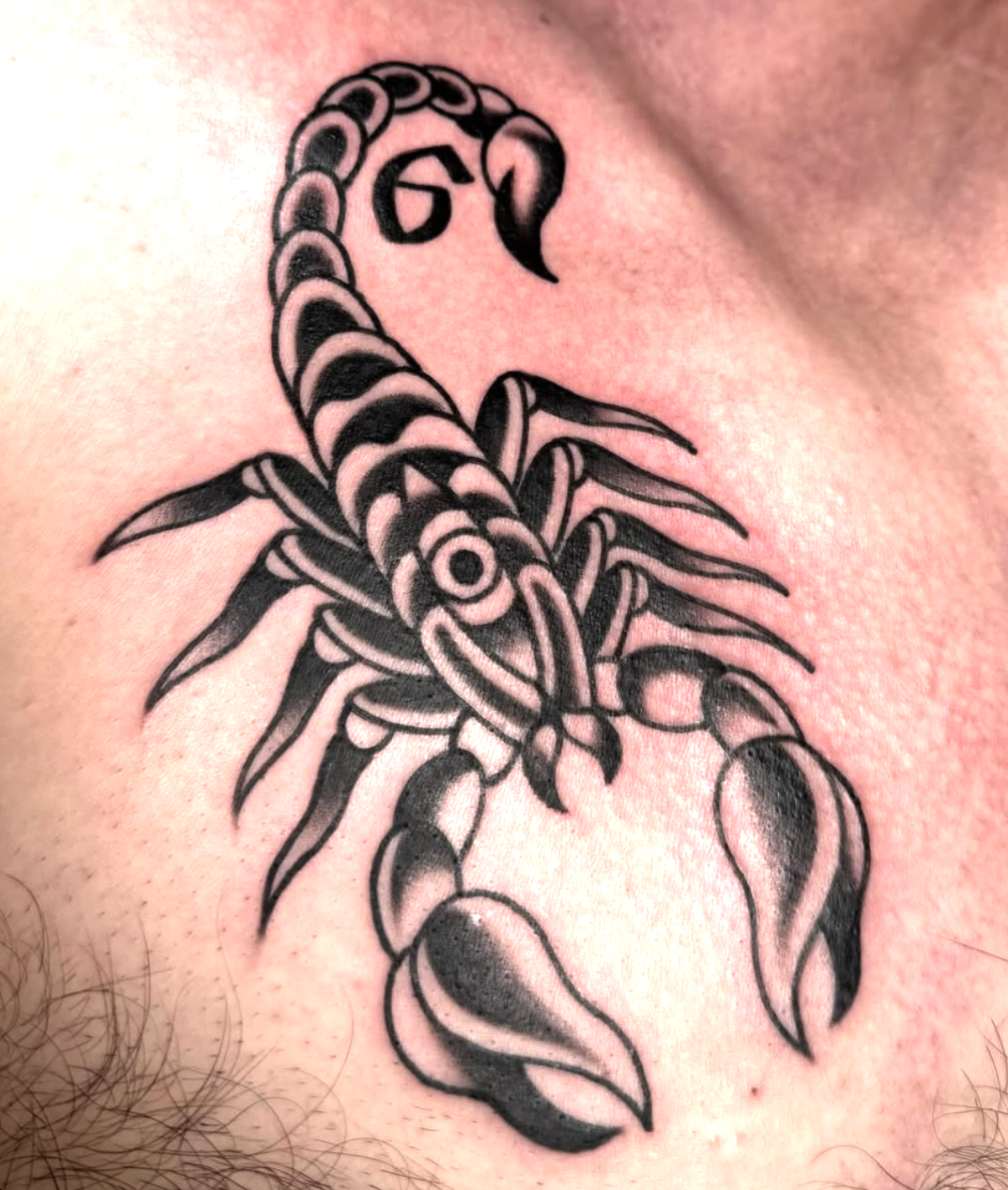 Tattoo of a stylized scorpion with bold black lines on skin.