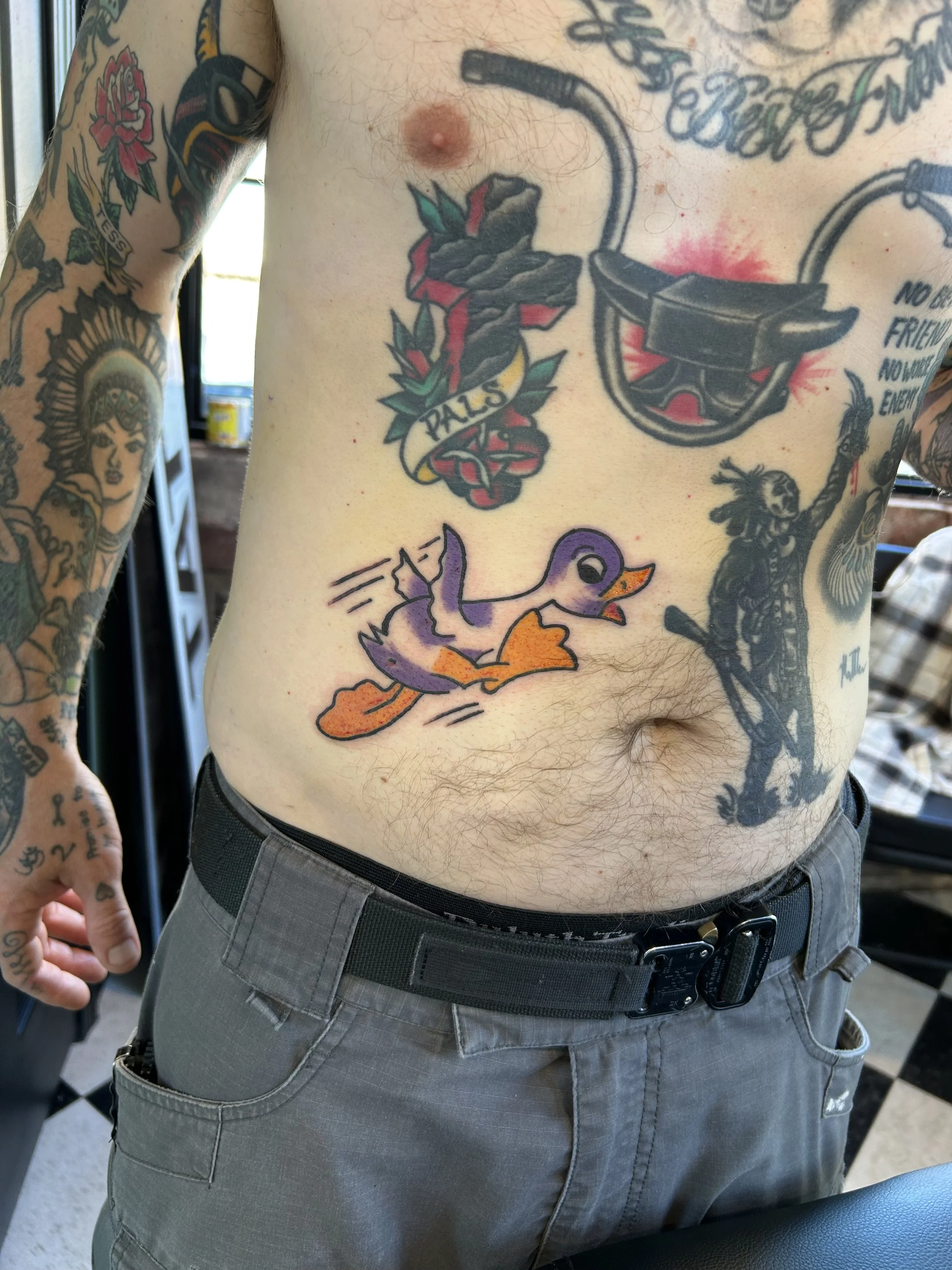 Chest tattoo of a rubber duck with purple wings and orange feet, in a cartoon style.