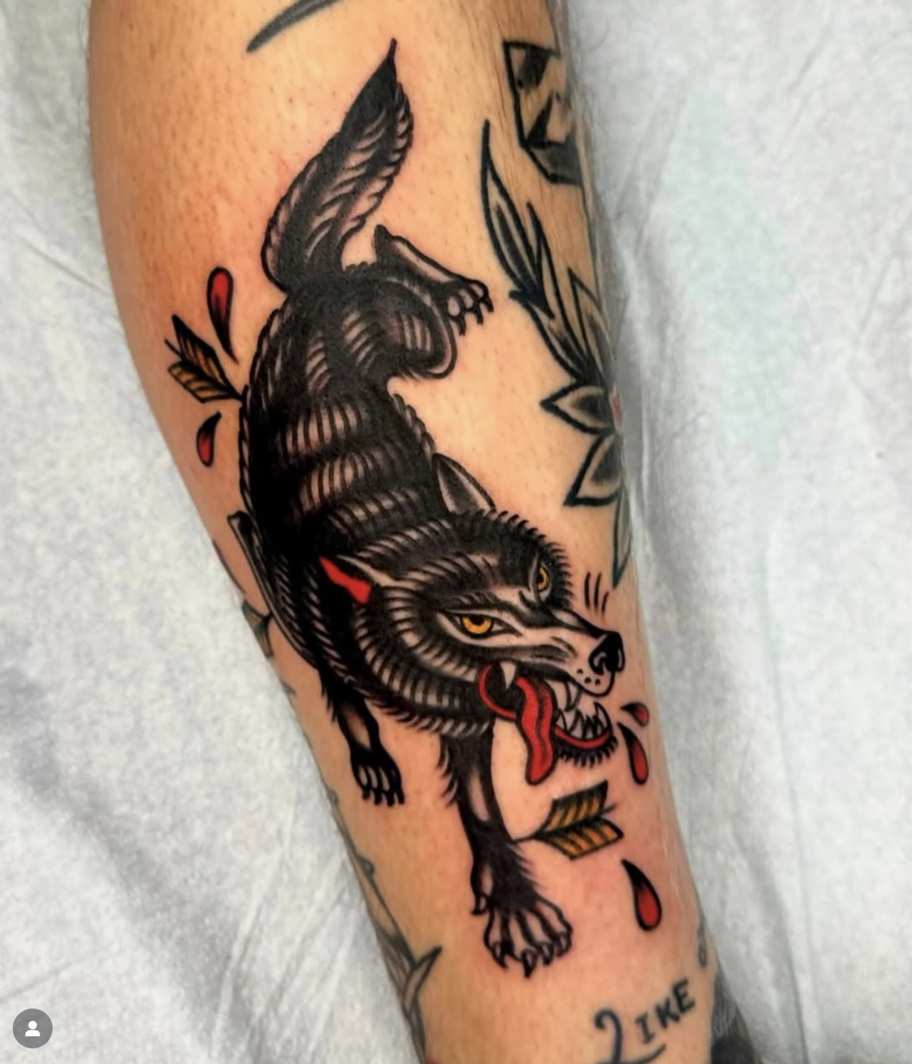 Tattoo of a snarling wolf with yellow eyes, red tongue, and blood drops on the arm.