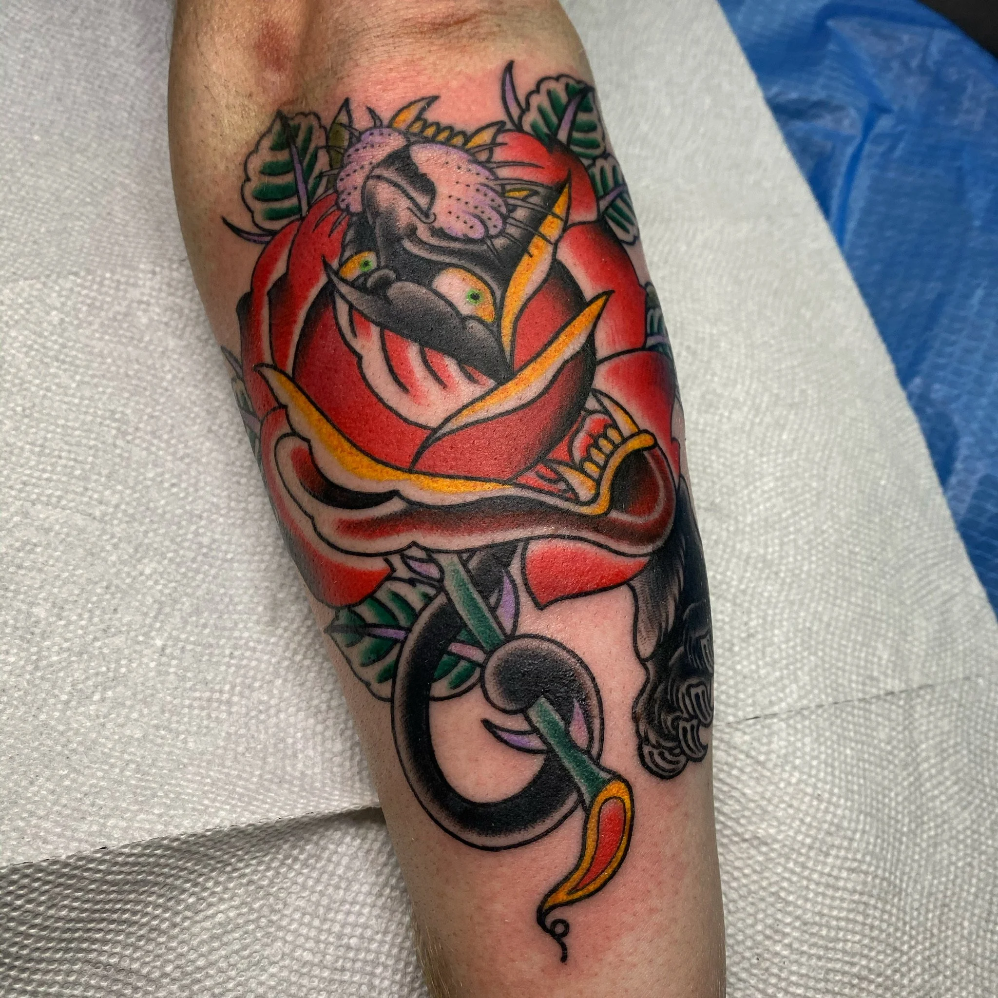 A colorful tattoo of a lion's face inside a red rose with green leaves and a black and yellow snake intertwined around it.